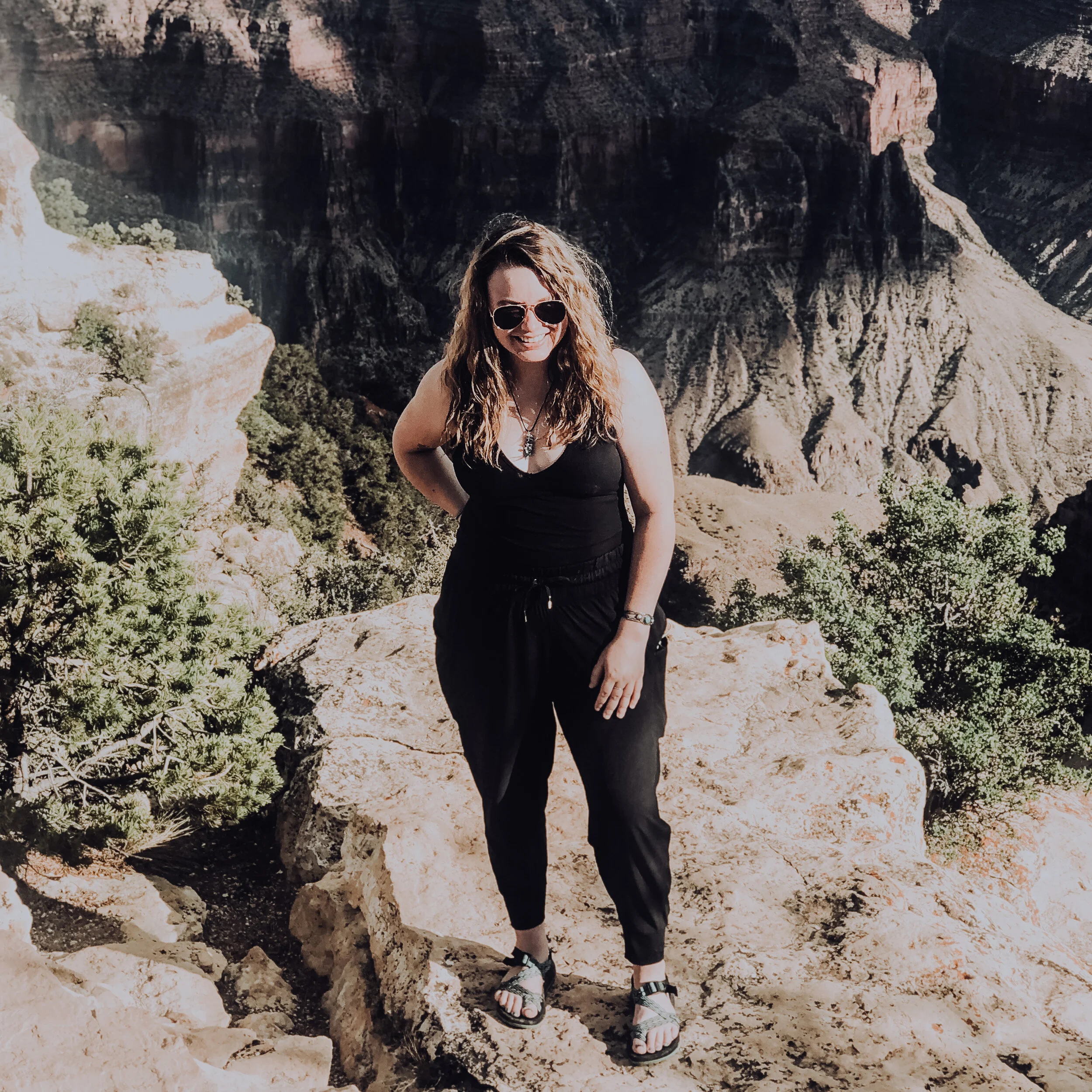 A photo of Cat standing on a rock in front of what appears to be a steep drop-off into a canyon.