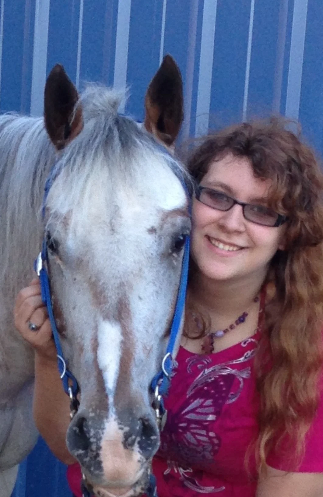 A photo of Christy and a horse against a blue metal building.