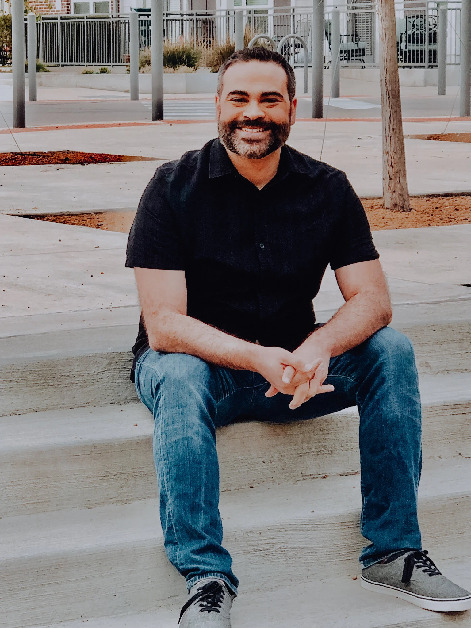 A photo of Don sitting on a sidewalk step with his hands folded in front of him.