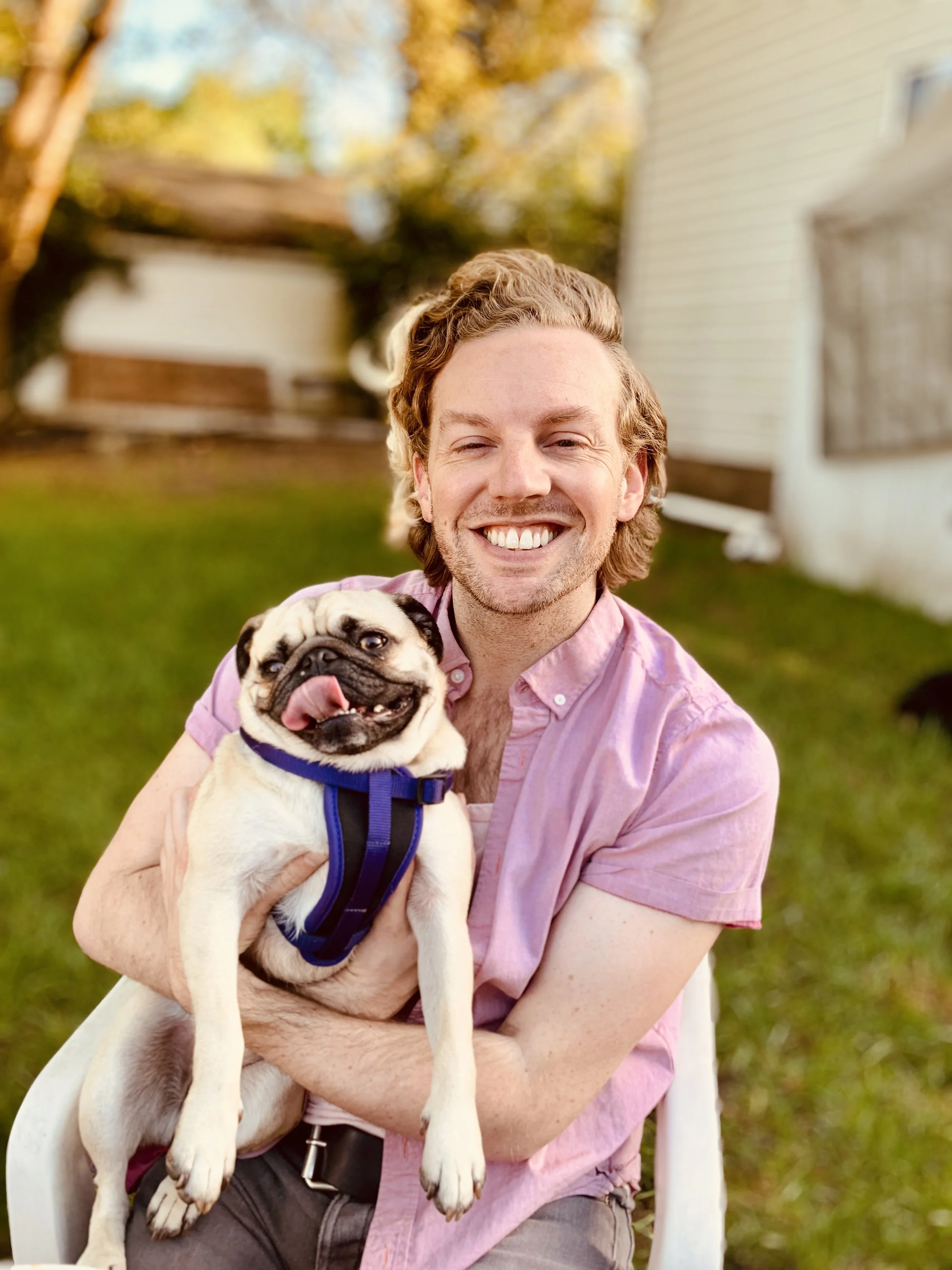 A photo of Drew holding a pug in his arms and smiling at the camera.