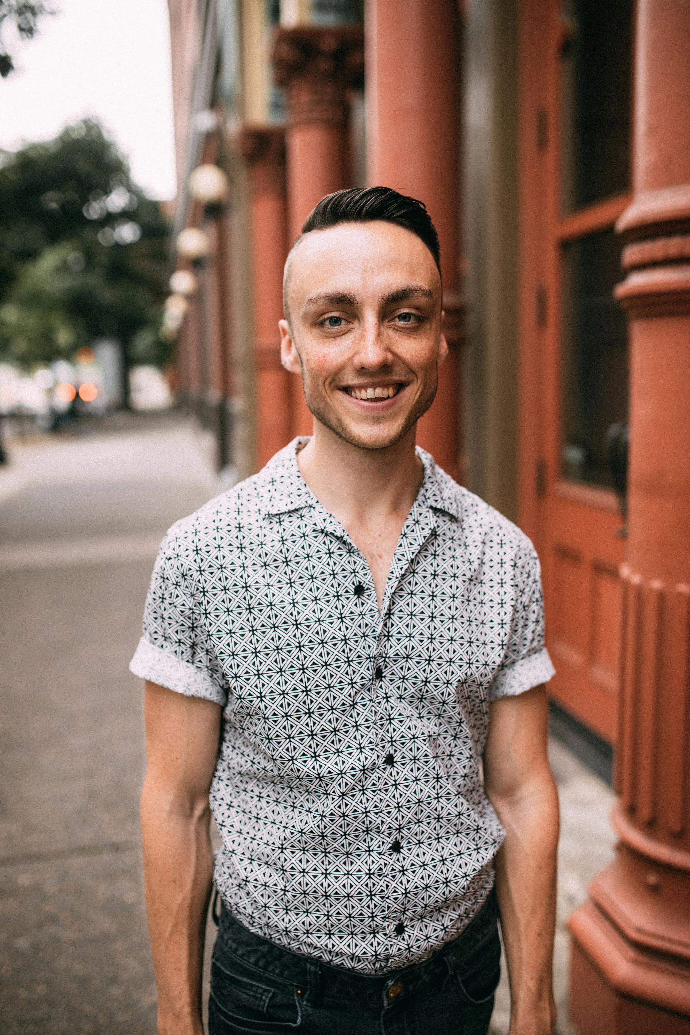 A photo of Gary in a button-down, standing on a sidewalk with a red building to his left.