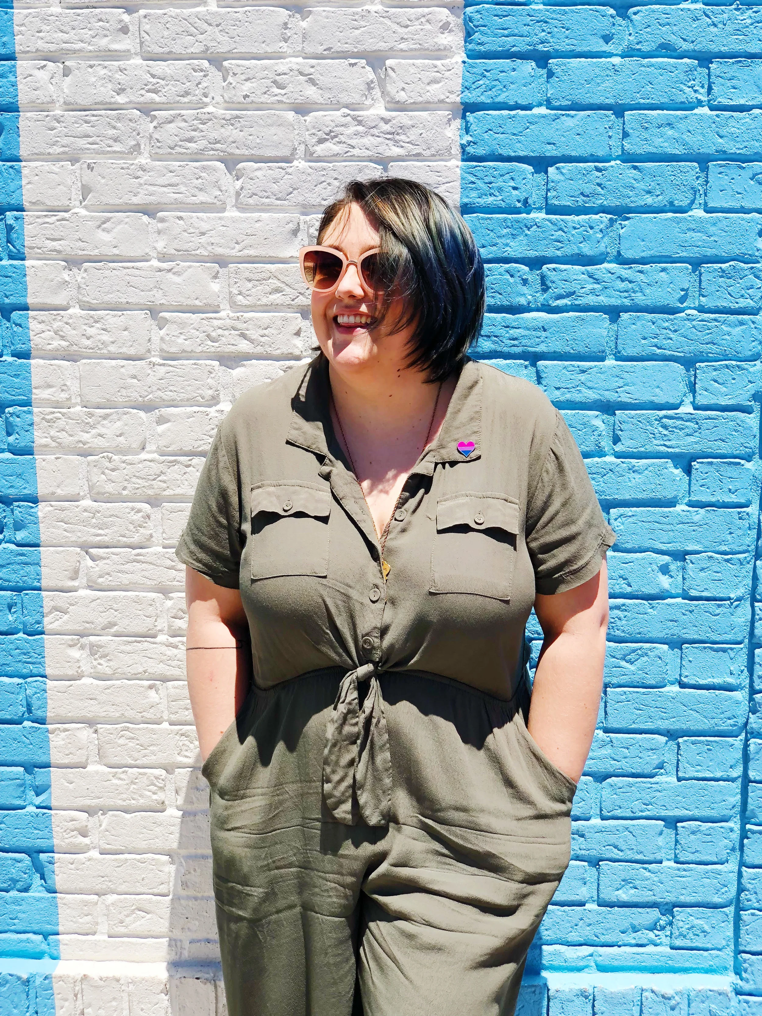 A photo of Haley in a green jumpsuit standing in front of a blue and white-striped building.