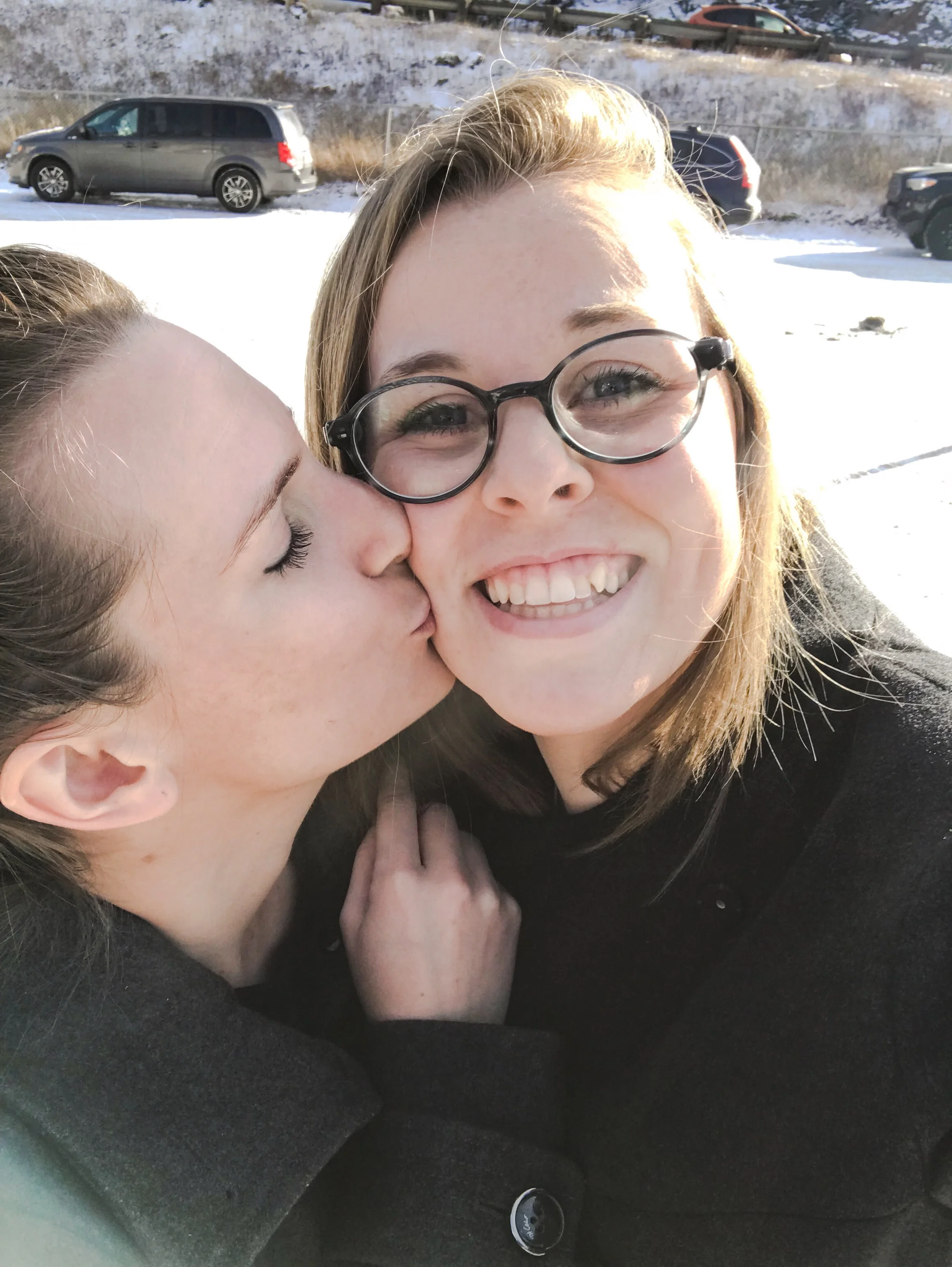 A photo of Lauren being kissed on the cheek by her partner Lauren in a snowy lot.
