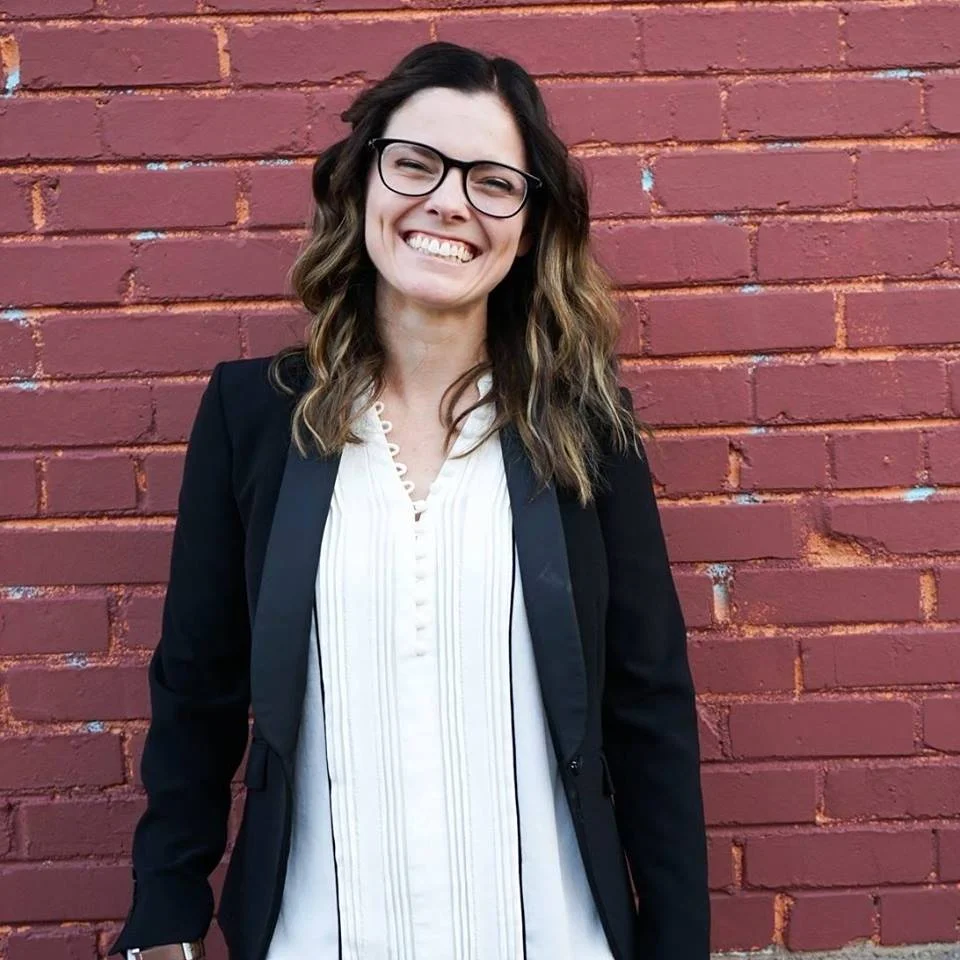 A photo of Heather smiling into the camera and standing in front of a brick wall.