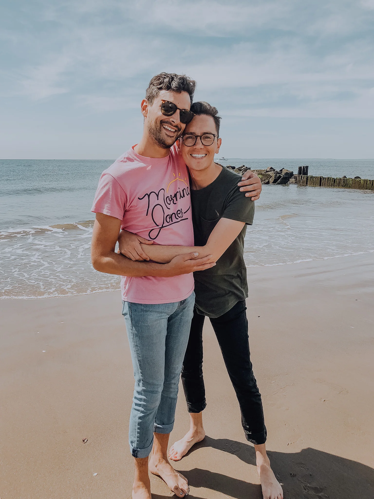A photo of Isaac hugging their partner on a beach.