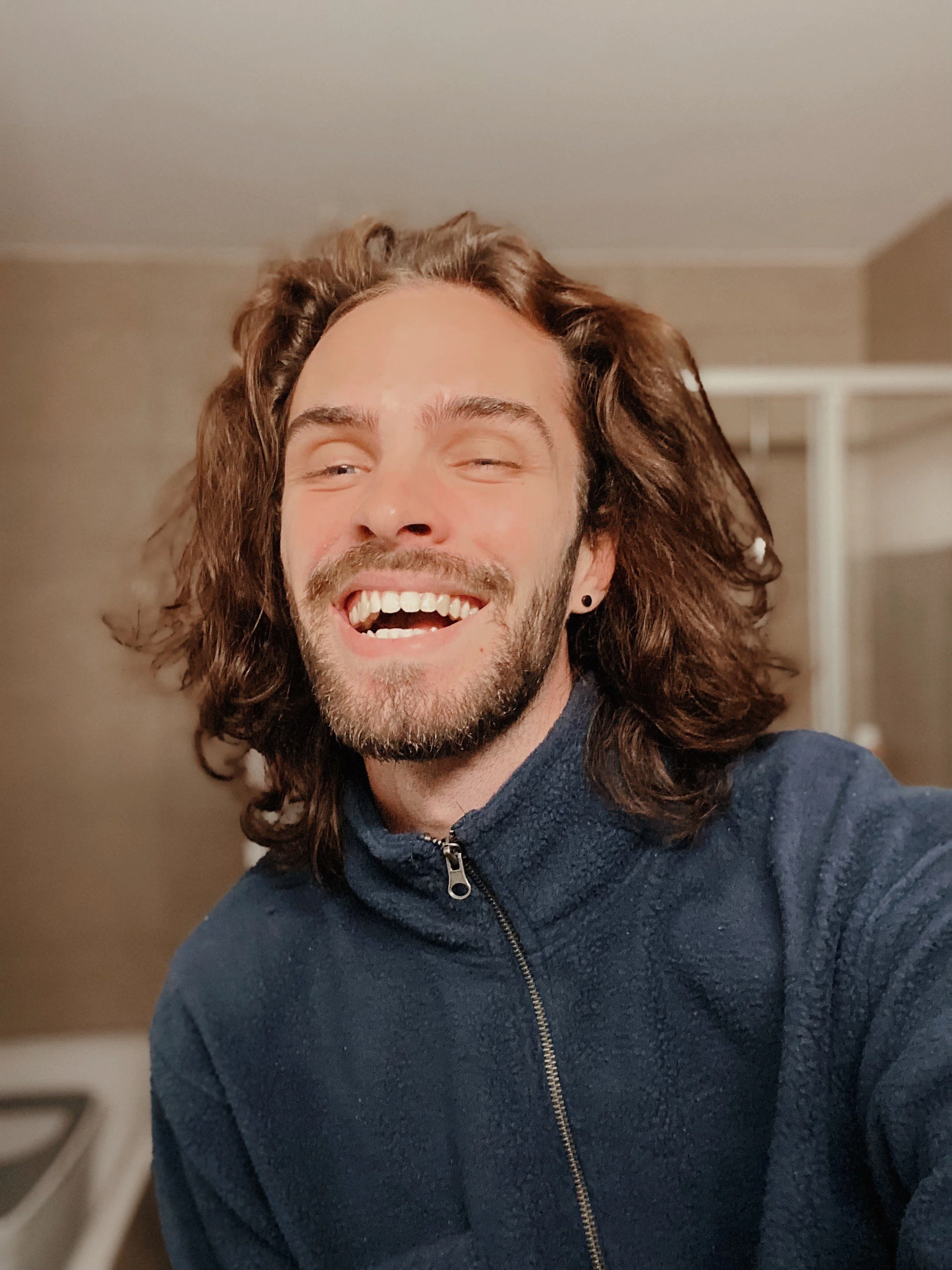 A photo of of Isaac laughing in a blue fleece sweater.