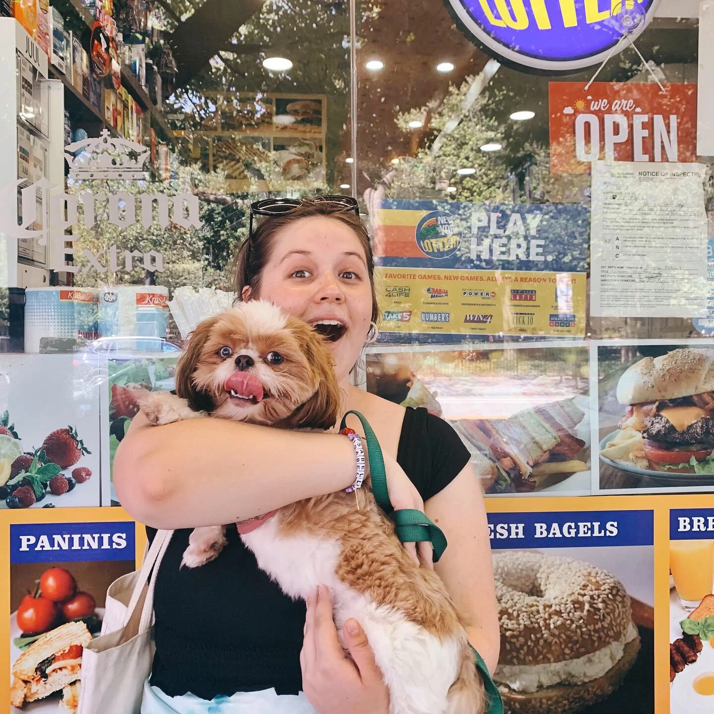 A photo of Isabella holding a dog in her arms standing in front of a deli's display window.