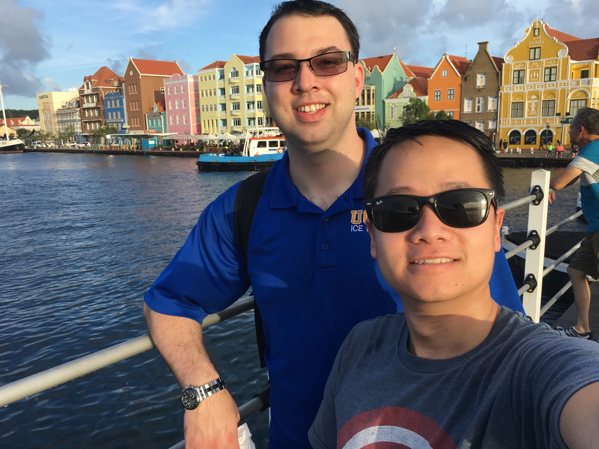 A photo of Jeremy and his husband in a European city with colorful buildings, a river, and boats in the background.