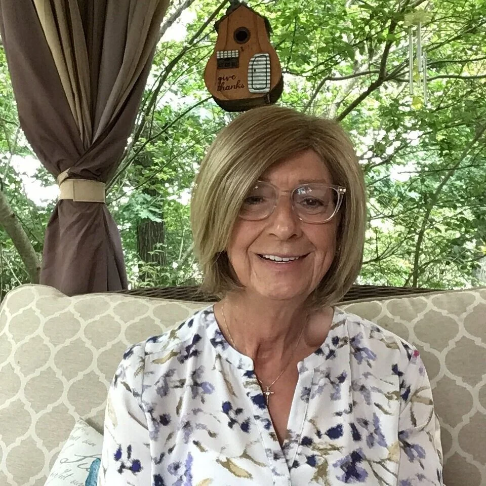 A photo of Kelly on a porch bench withe foliage behind her.