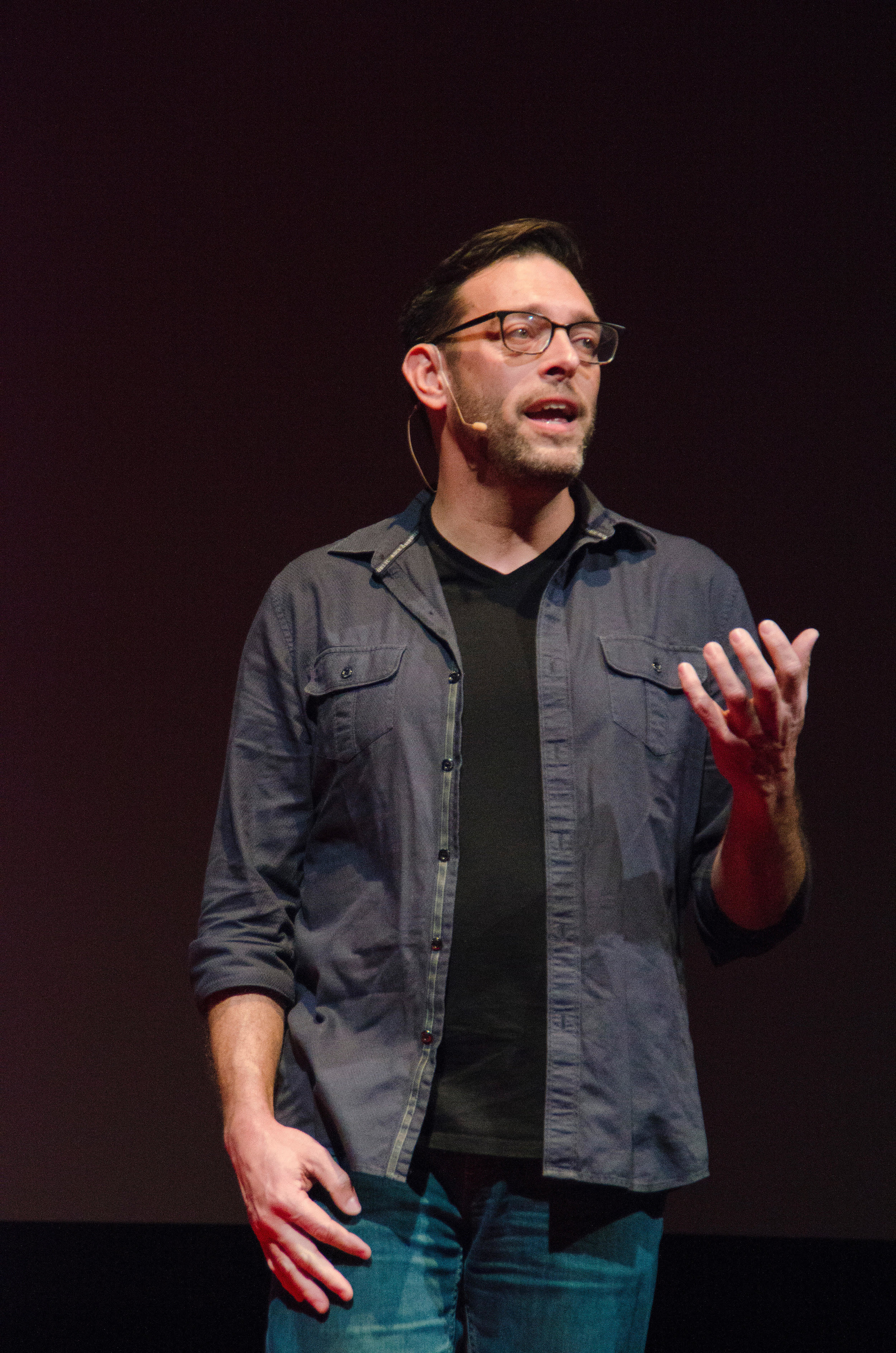 A photo of Matt speaking on stage in a grey button-down, black t-shirt, with a mic around his right ear.