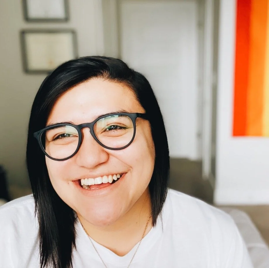 A photo of Noemi smiling into the camera with a pride flag in the background.