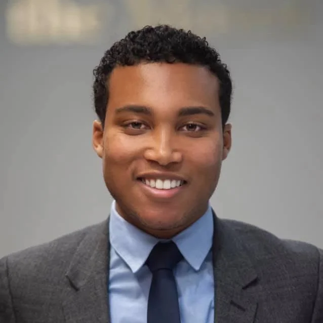 A photo of Ralph in a suit and blue shirt, blue tie, against a blurred background.