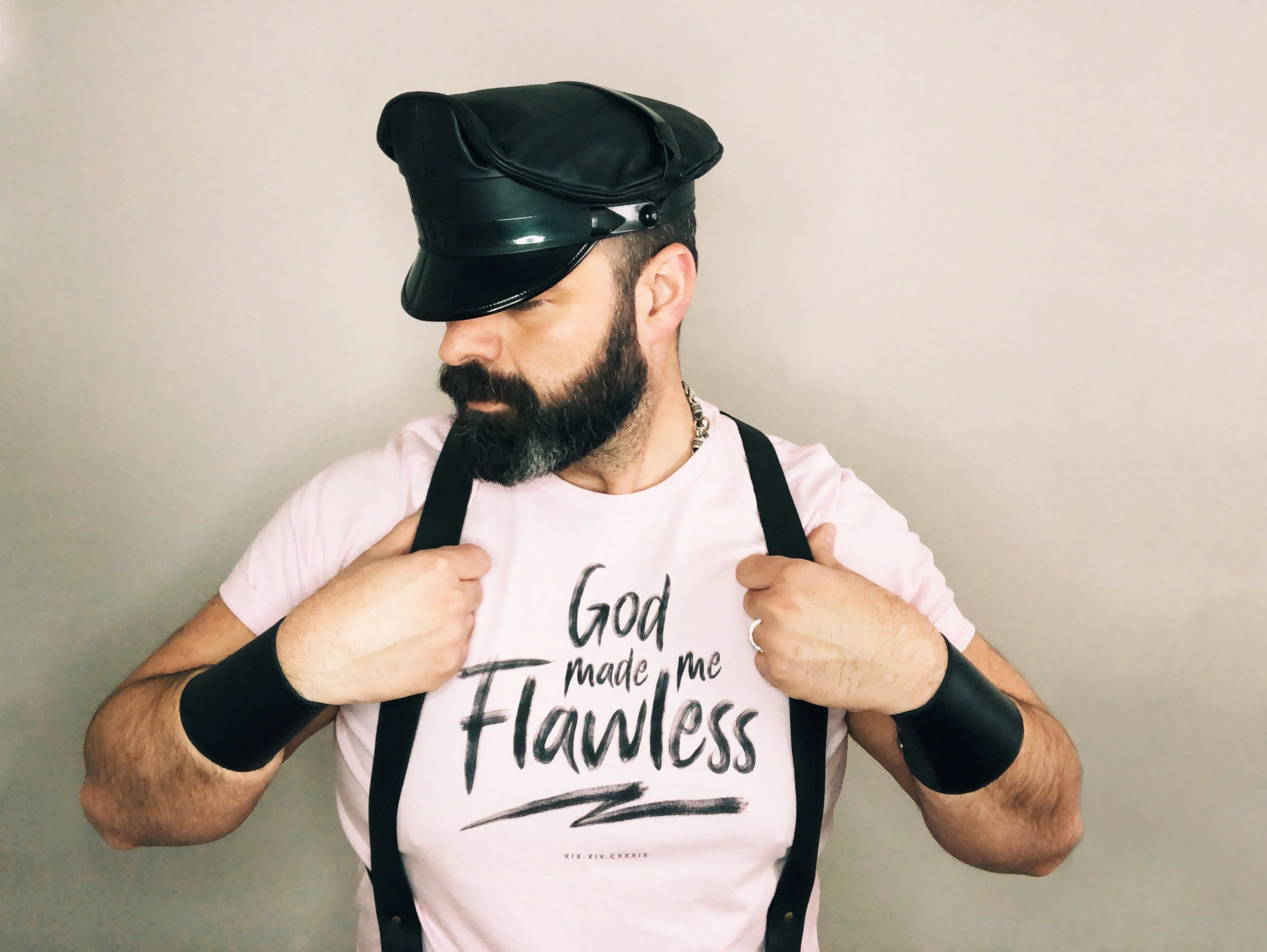 A photo of Robert wearing a black hat, black wrist cuffs, suspenders, and a pink shirts which reads "God made me flawless" in script.