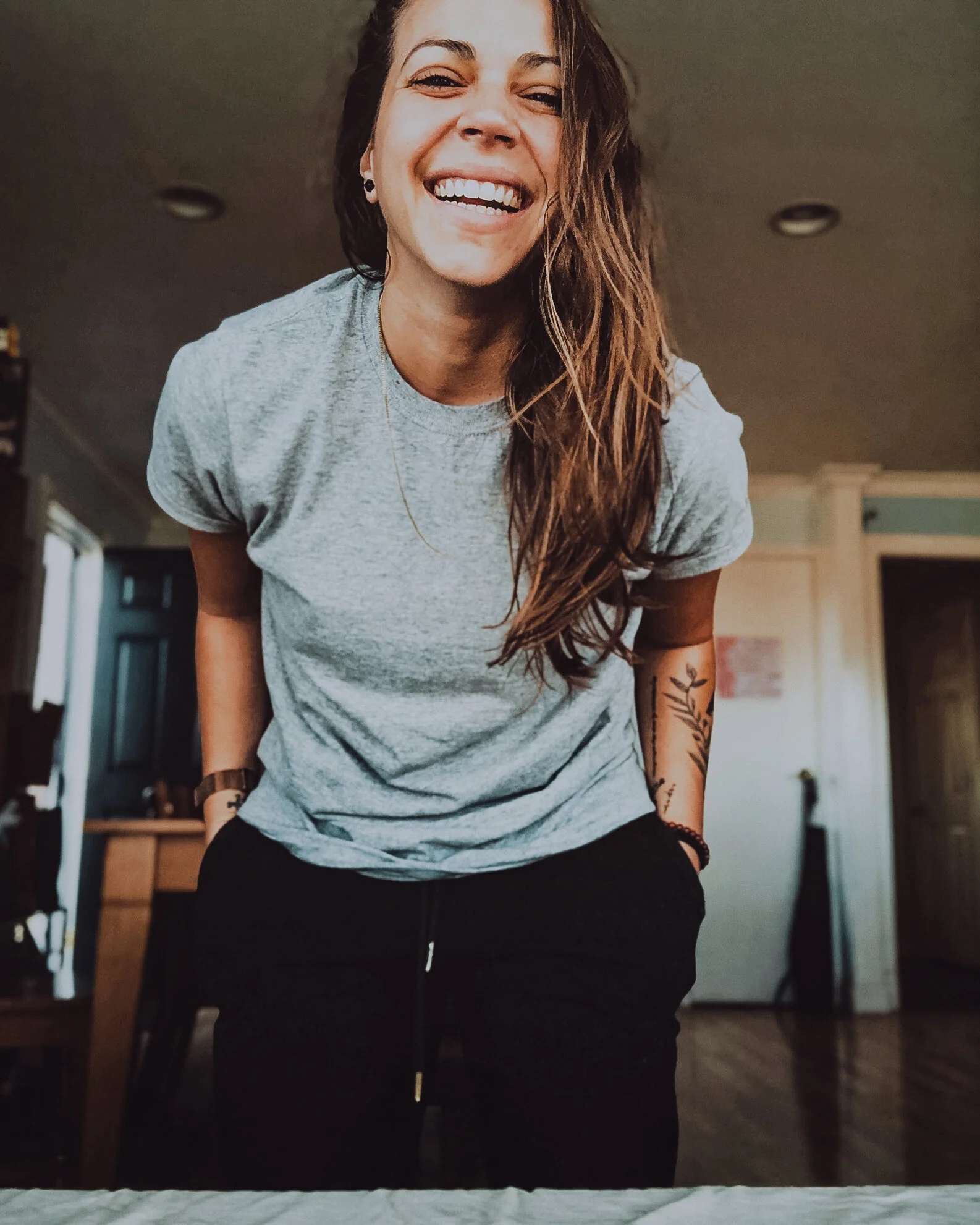 A photo of Stefie smiling in a t-shirt, leaning down towards the camera with her hands in her pocket.