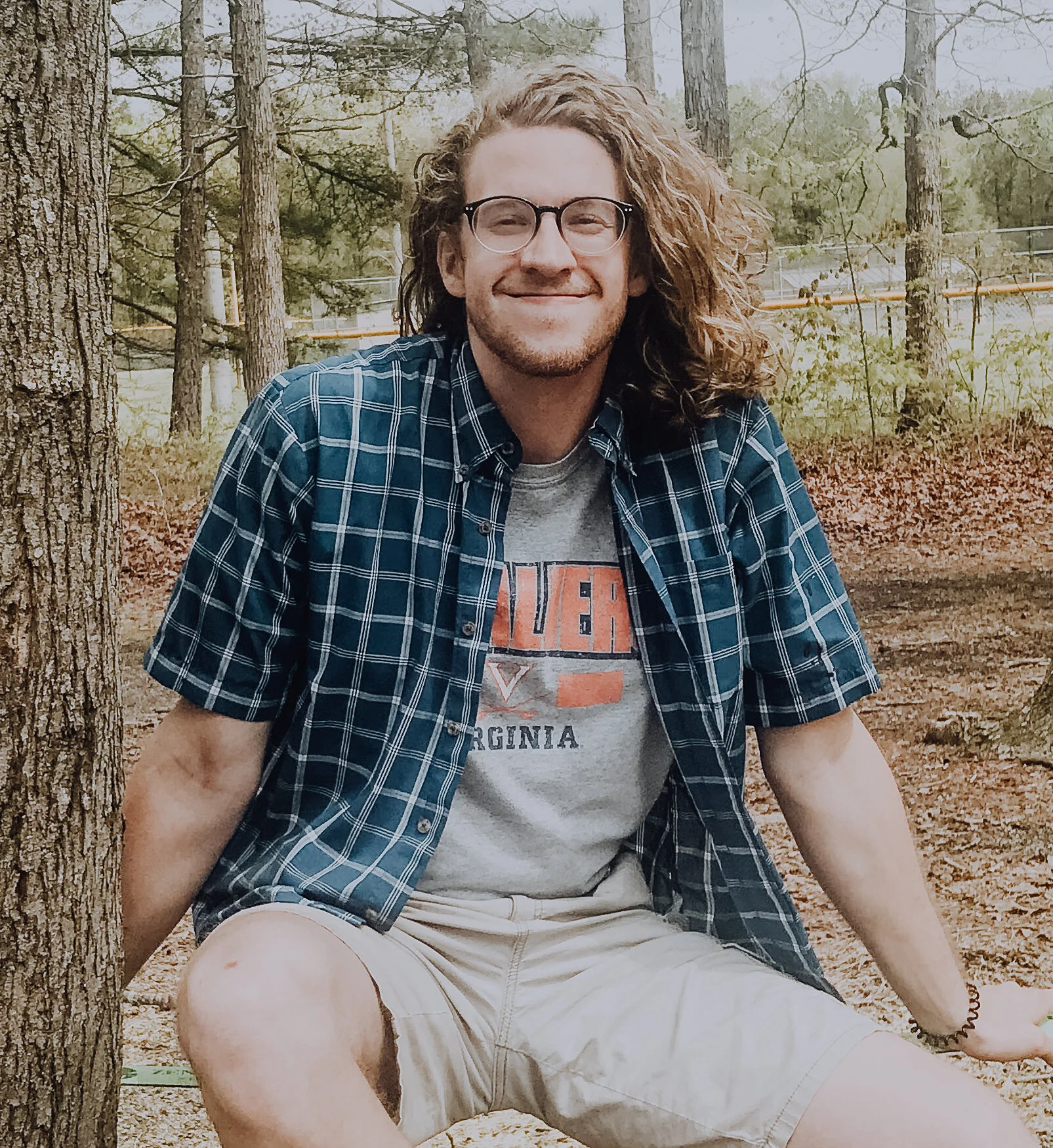 A photo of Tony wearing a UVA shirt and sitting next to a tree with a fence in the background.