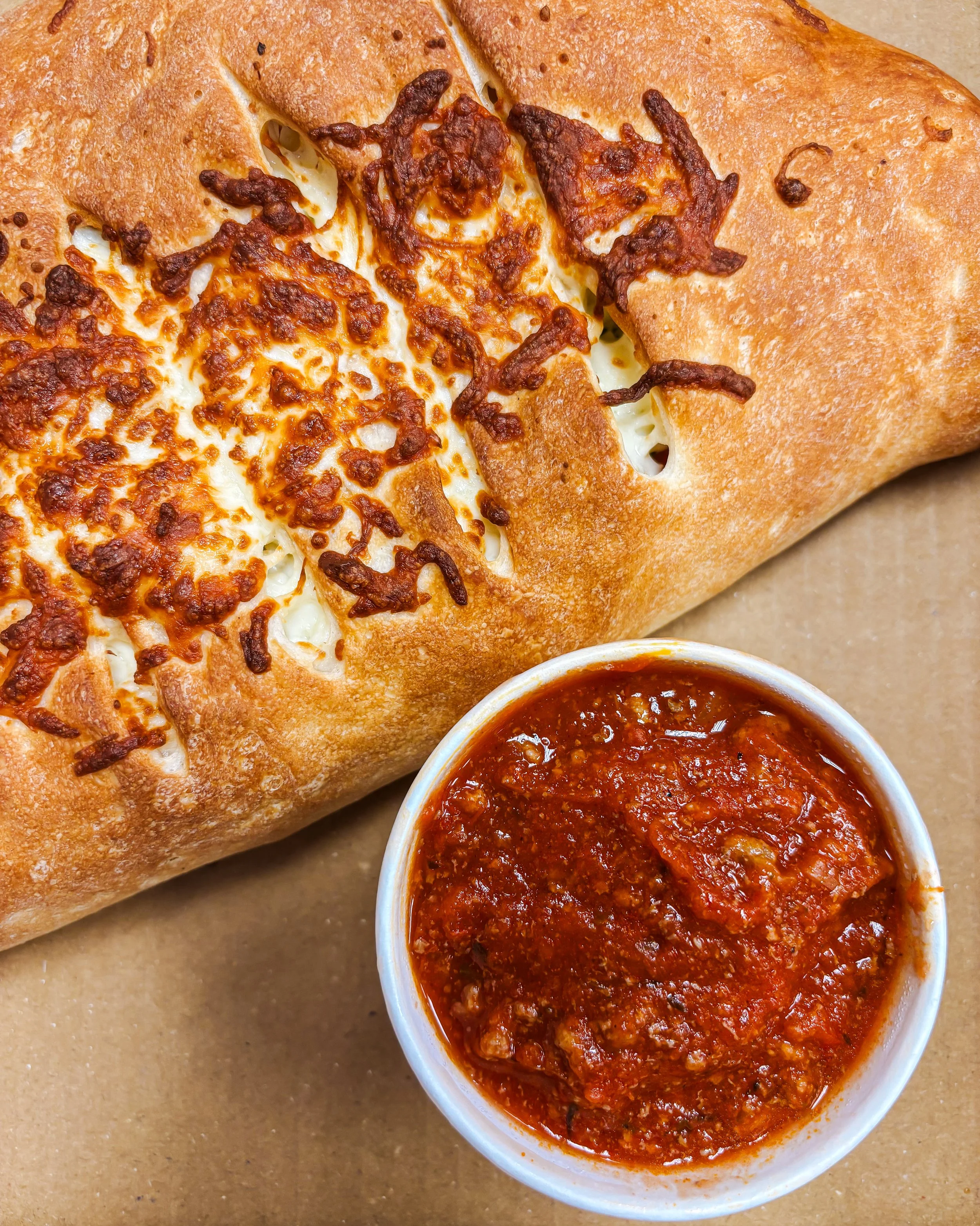 A panzerotti topped with cheese and a side of marinara meat sauce in a white bowl.