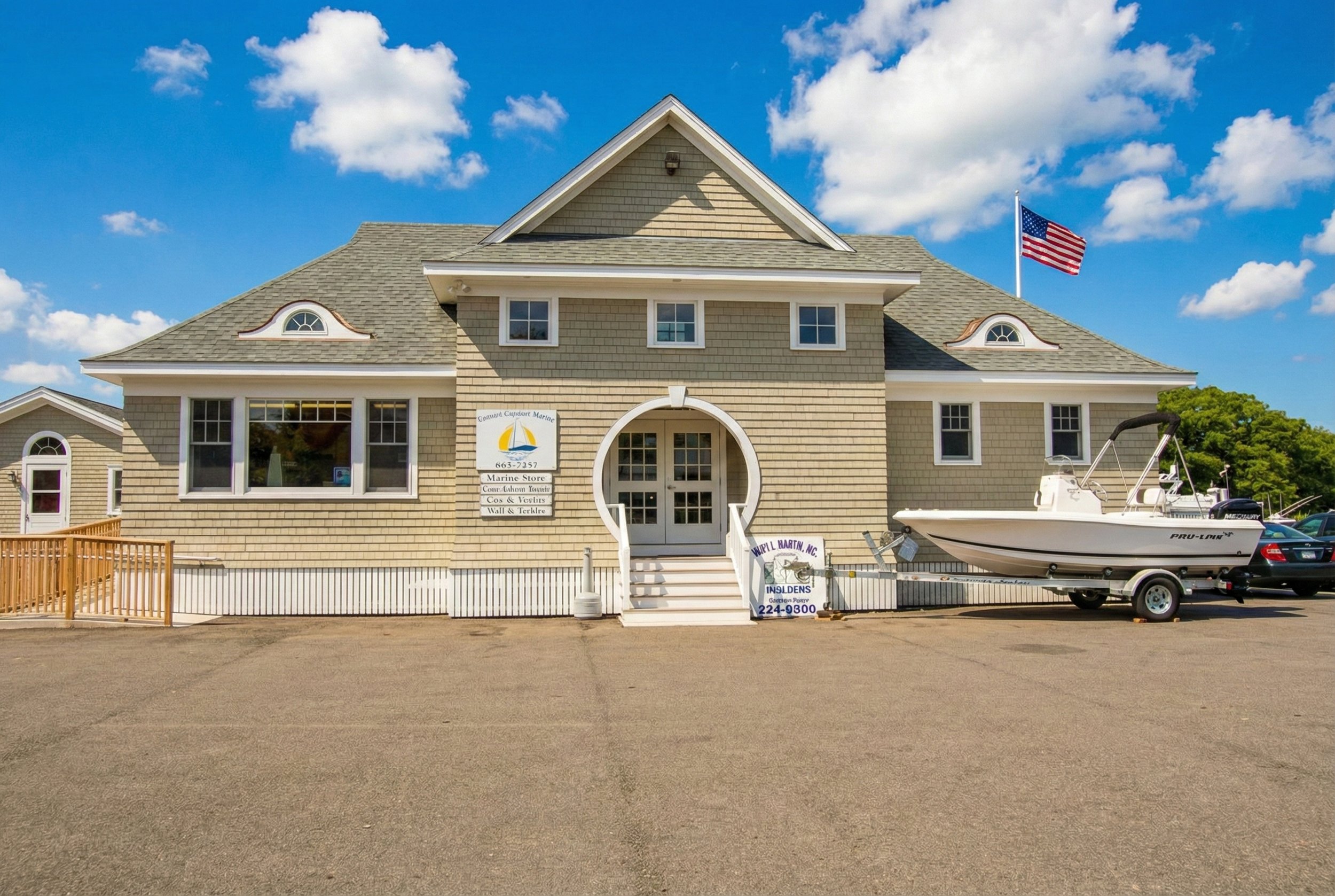 Building with a sign advertising a marine store, a boat on a trailer, and an American flag flying on a clear day with blue sky and clouds.
