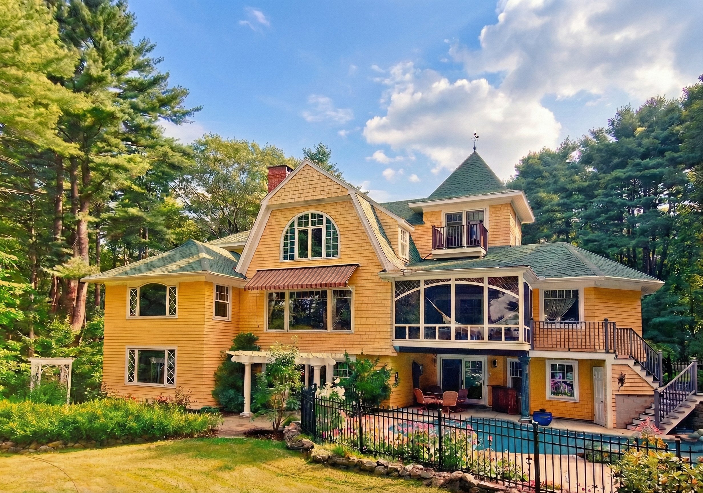 Large yellow Victorian-style house with multiple stories, green roof, and a small outdoor pool, surrounded by trees and landscaped garden under a partly cloudy sky.