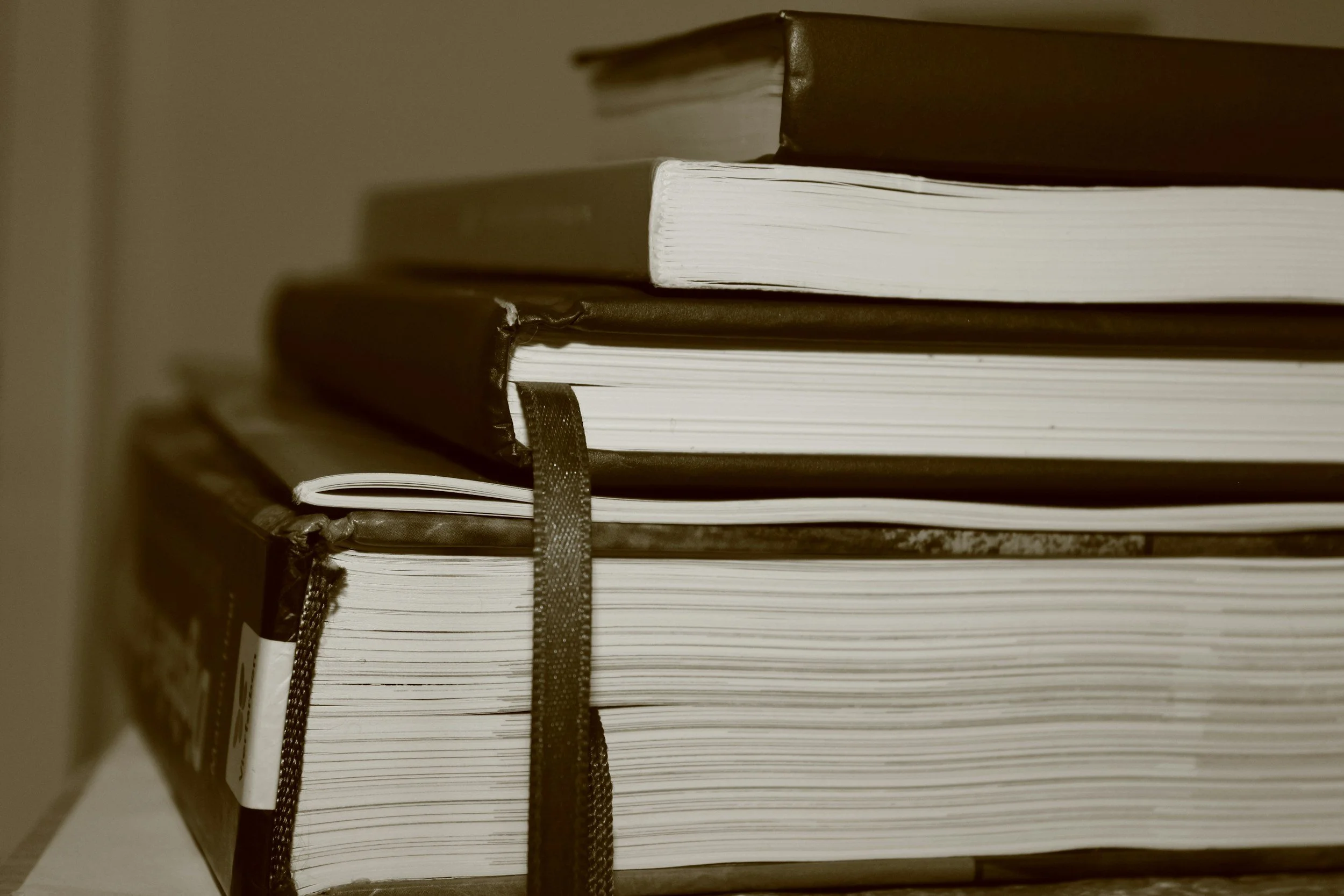 Stacked books and notebooks in sepia tone, with some with bookmarks and worn edges.