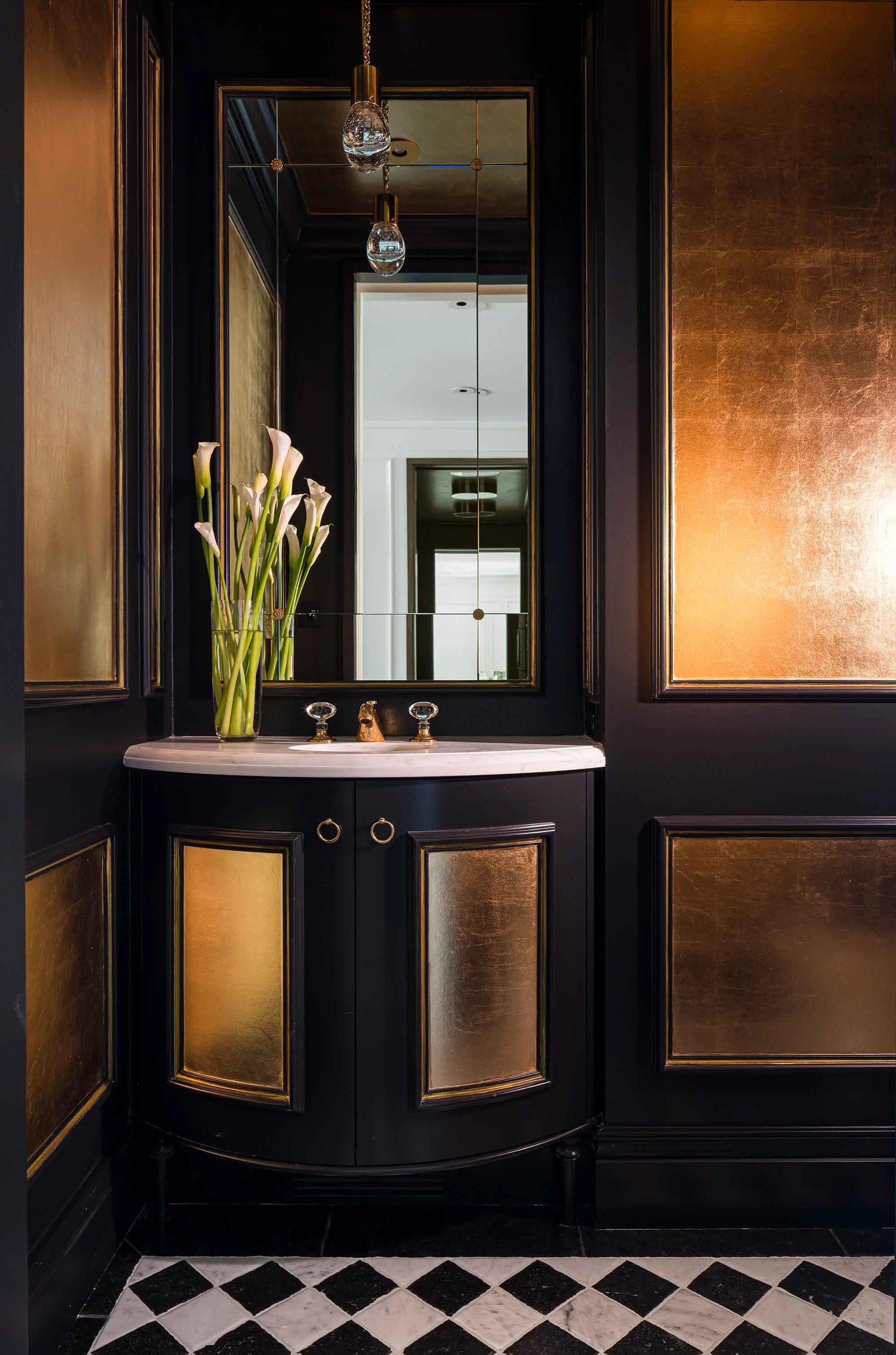 Dramatic powder room with black and gold leaf paneled walls, curved black vanity with gold accents, and harlequin marble floor 