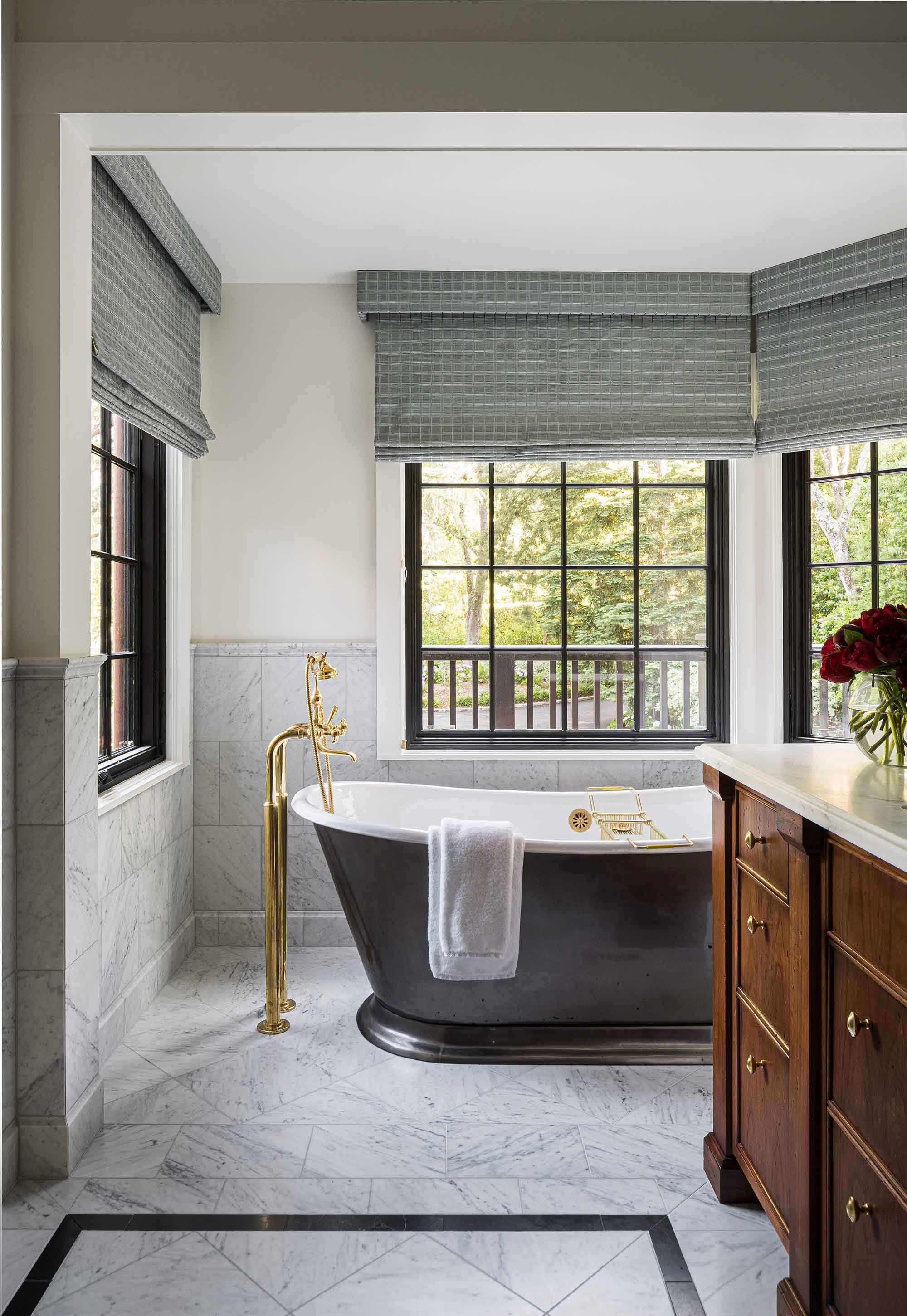 Primary bathroom with freestanding dark soaking tub, brass floor mount faucet, Calacatta marble tile floors and walls