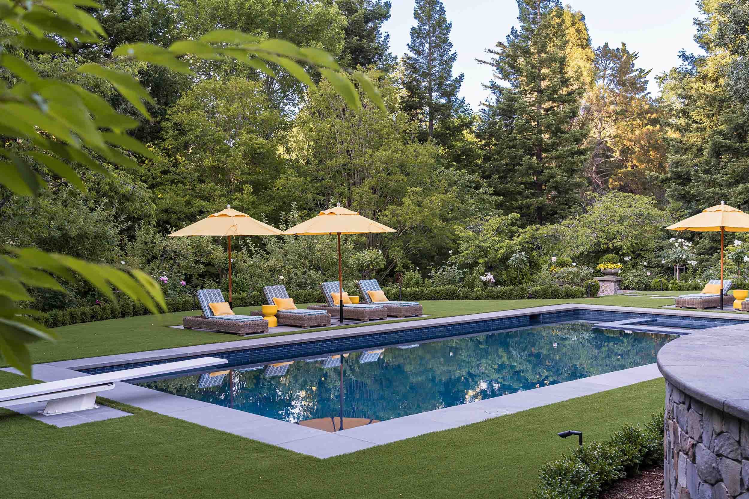 Luxury swimming pool with lounge chairs and yellow umbrellas surrounded by manicured lawn and lush gardens