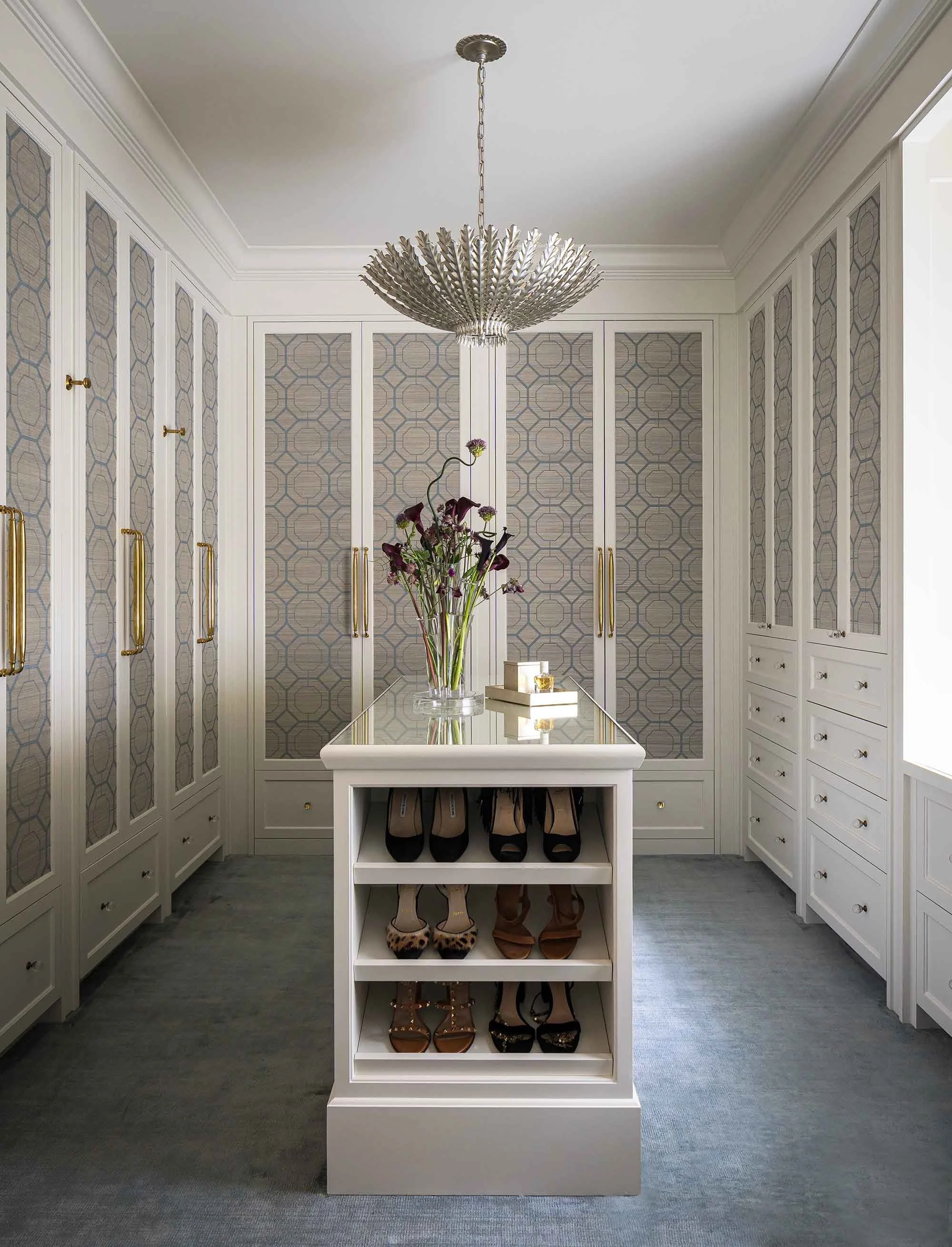 Custom walk-in closet with floor-to-ceiling cabinetry, patterned glass front doors, center shoe island, and statement pendant