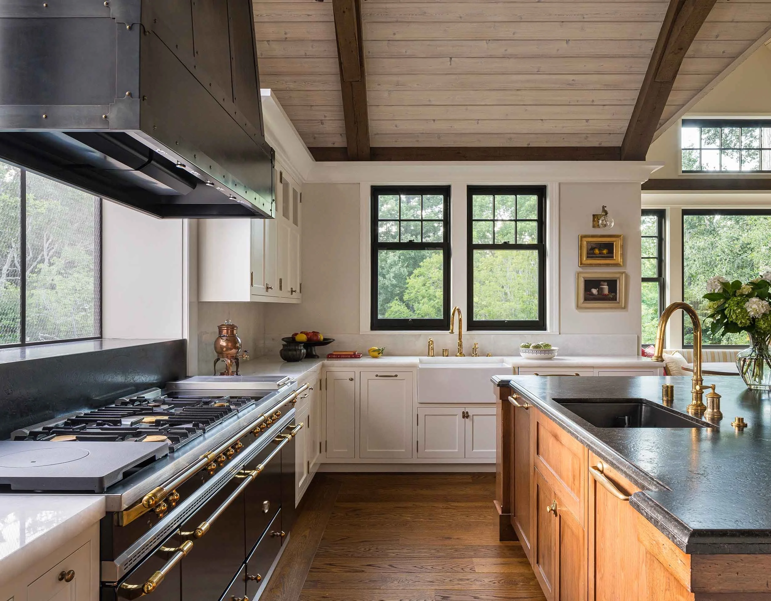Chef's kitchen with La Cornue range, custom black steel hood, walnut island with stone countertop, brass fixtures, and black-framed
windows.