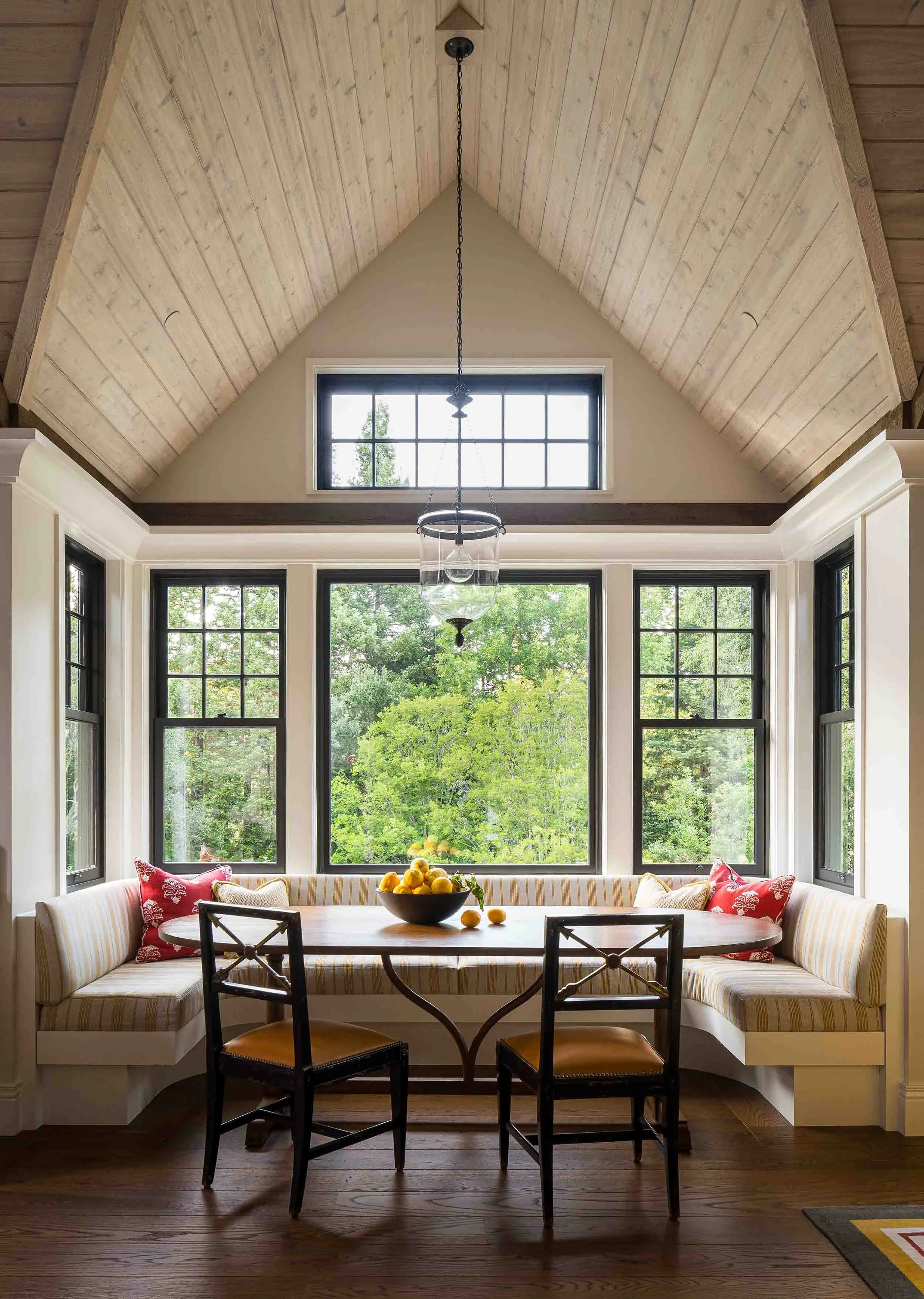 Breakfast nook with cathedral shiplap ceiling, built-in banquette seating, and wall of black-framed windows with garden views in
Norman Charles Construction custom home.