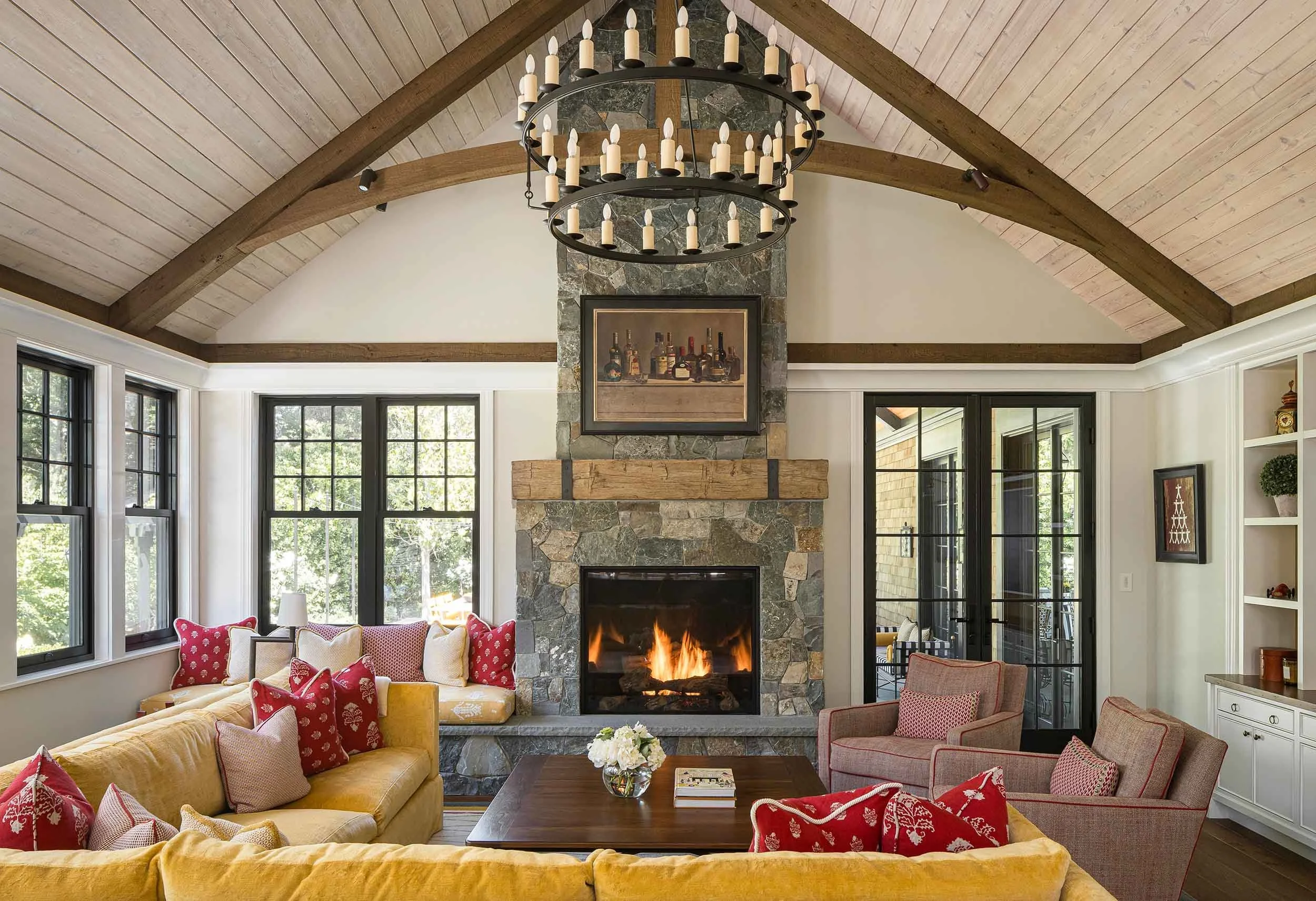 Great room with vaulted ceiling, exposed timber beams, floor-to ceiling stone fireplace, and wrought iron candle chandelier