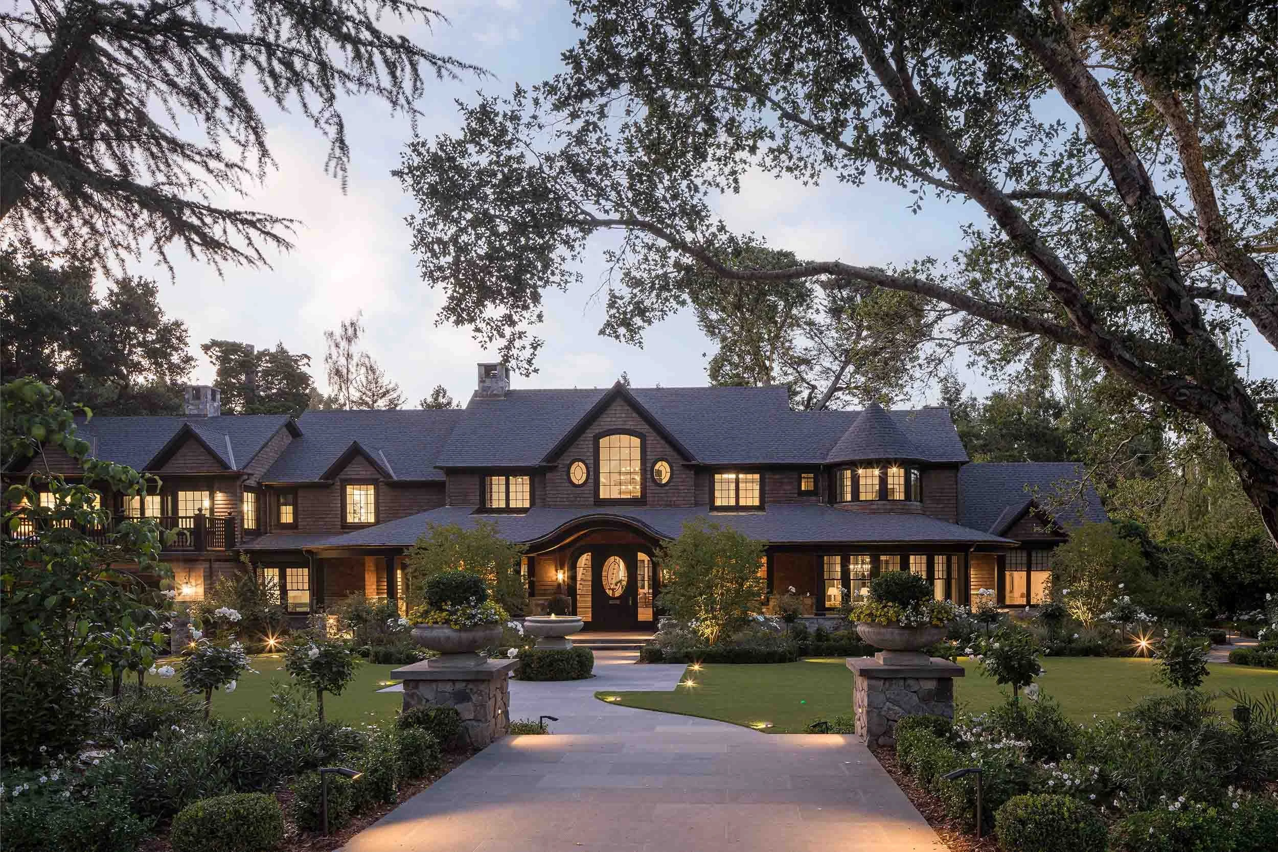 Evening driveway view of Norman Charles Construction luxury custom home with stone entrance pillars, landscape lighting, and
manicured grounds