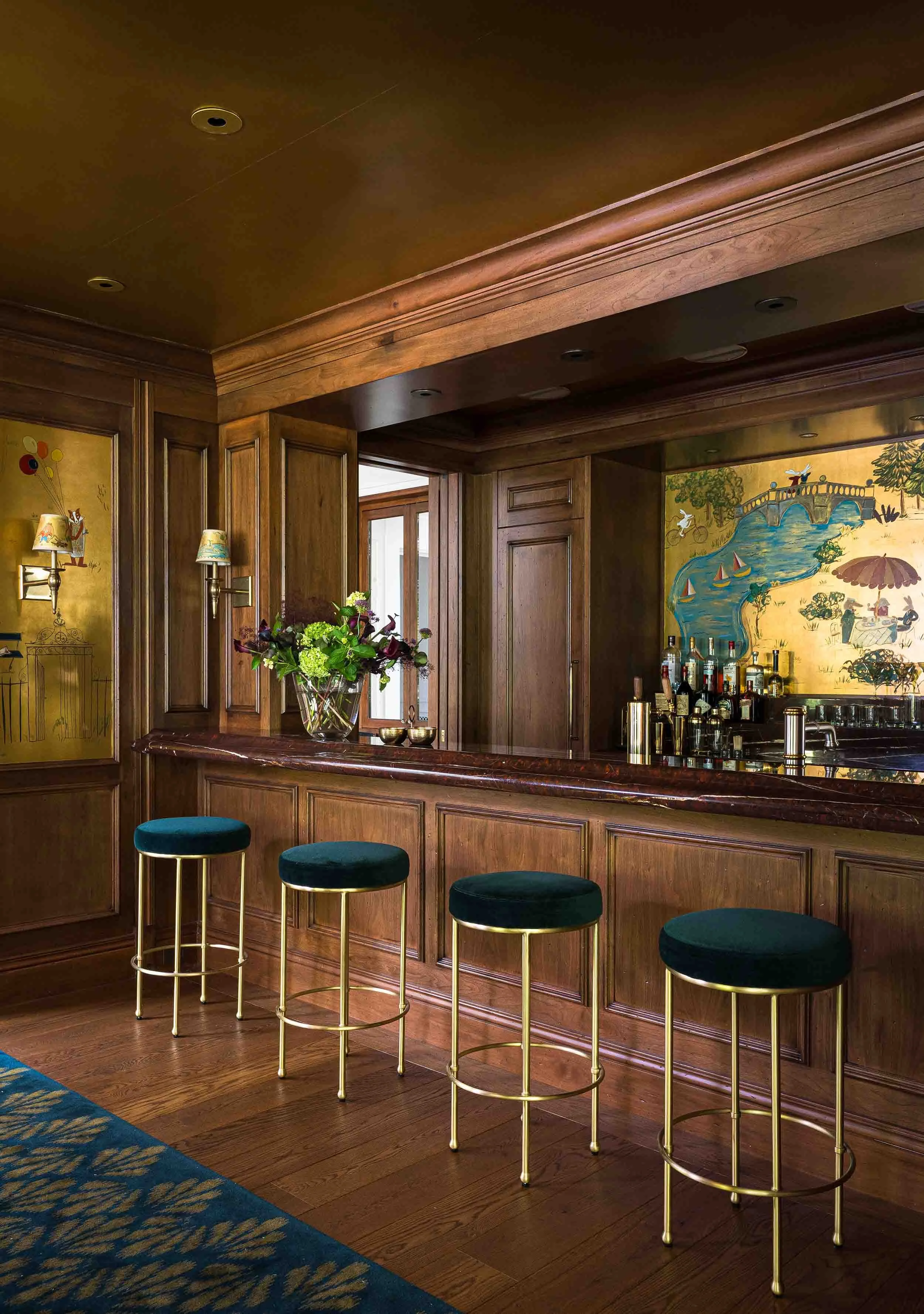 Custom walnut home bar with dark stone countertop, chinoiserie mural backsplash, and brass accents with velvet bar stools