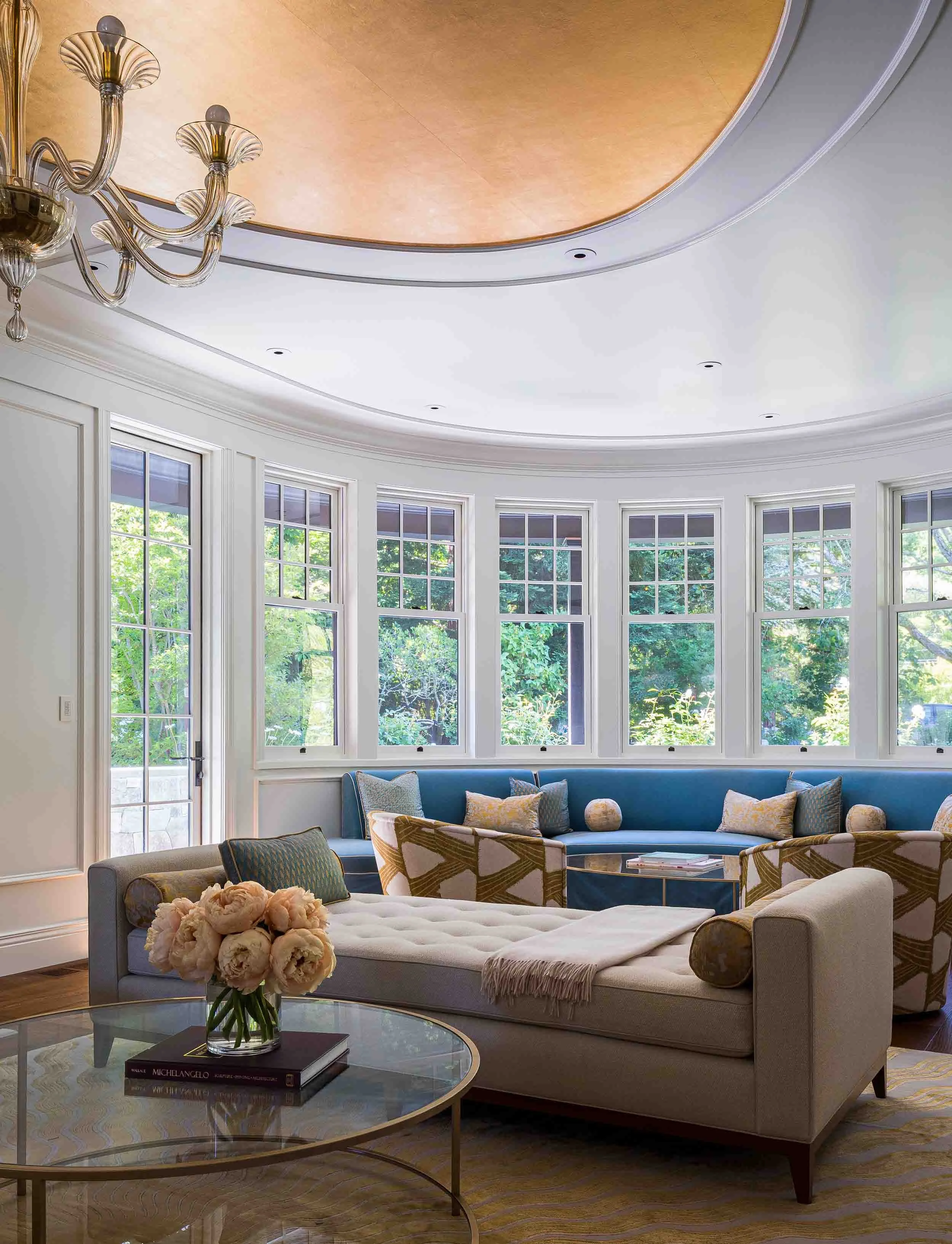 Circular living room with curved window wall, gold leaf coffered dome ceiling, blue built-in window seat, and Murano chandelier 