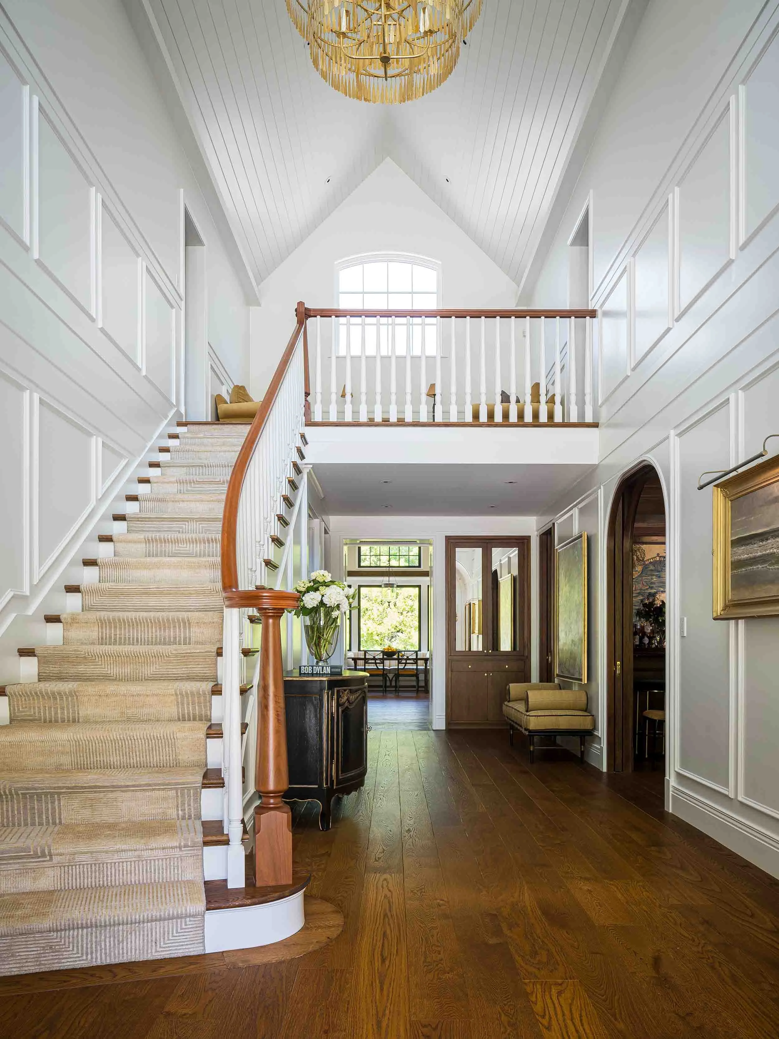 Grand foyer with sweeping curved staircase, custom paneled wainscoting, soaring vaulted ceiling, and wide plank hardwood floors. 