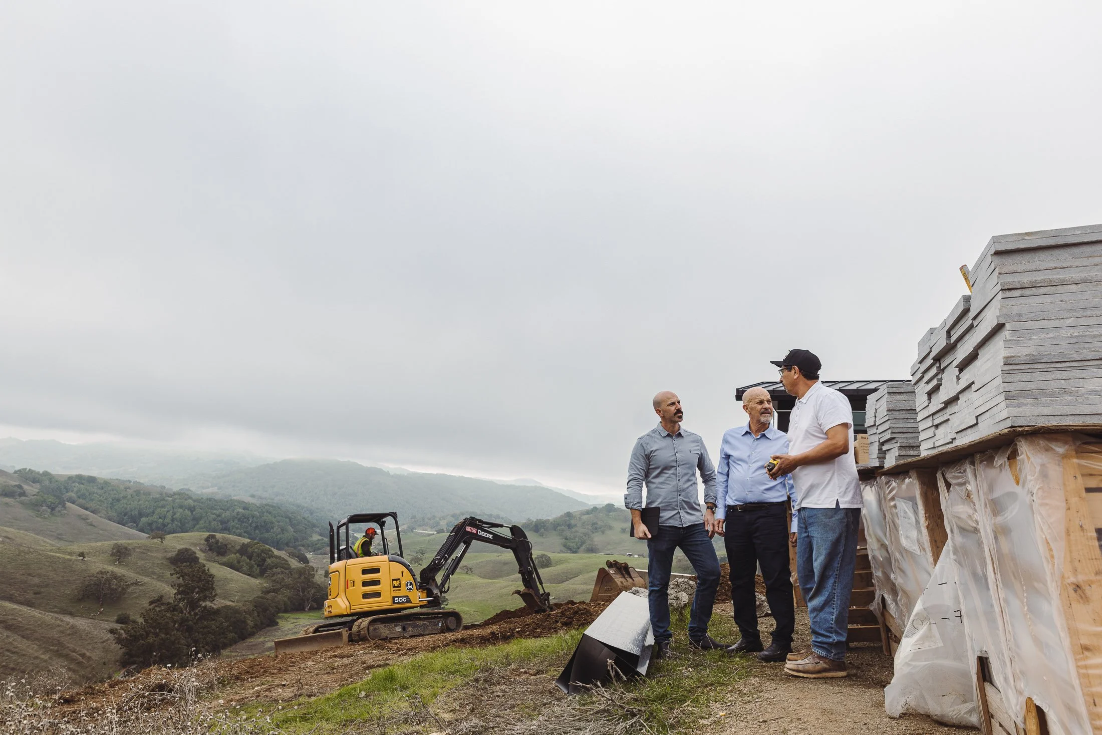 Norman Charles Construction team reviewing plans at a hillside custom home build site with excavation equipment.