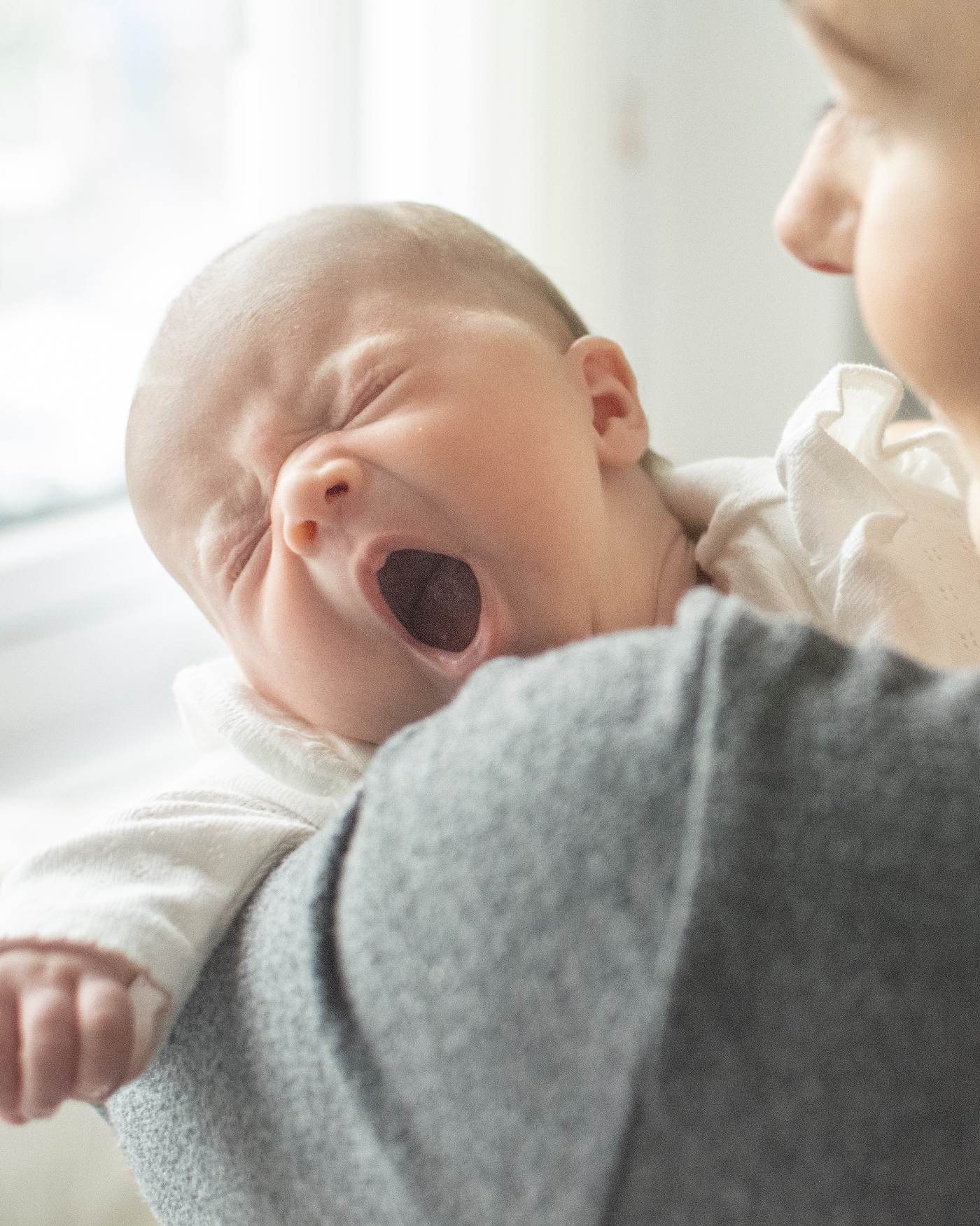 A person holding a yawning baby close to their face, with the baby appearing to be tired or sleepy.