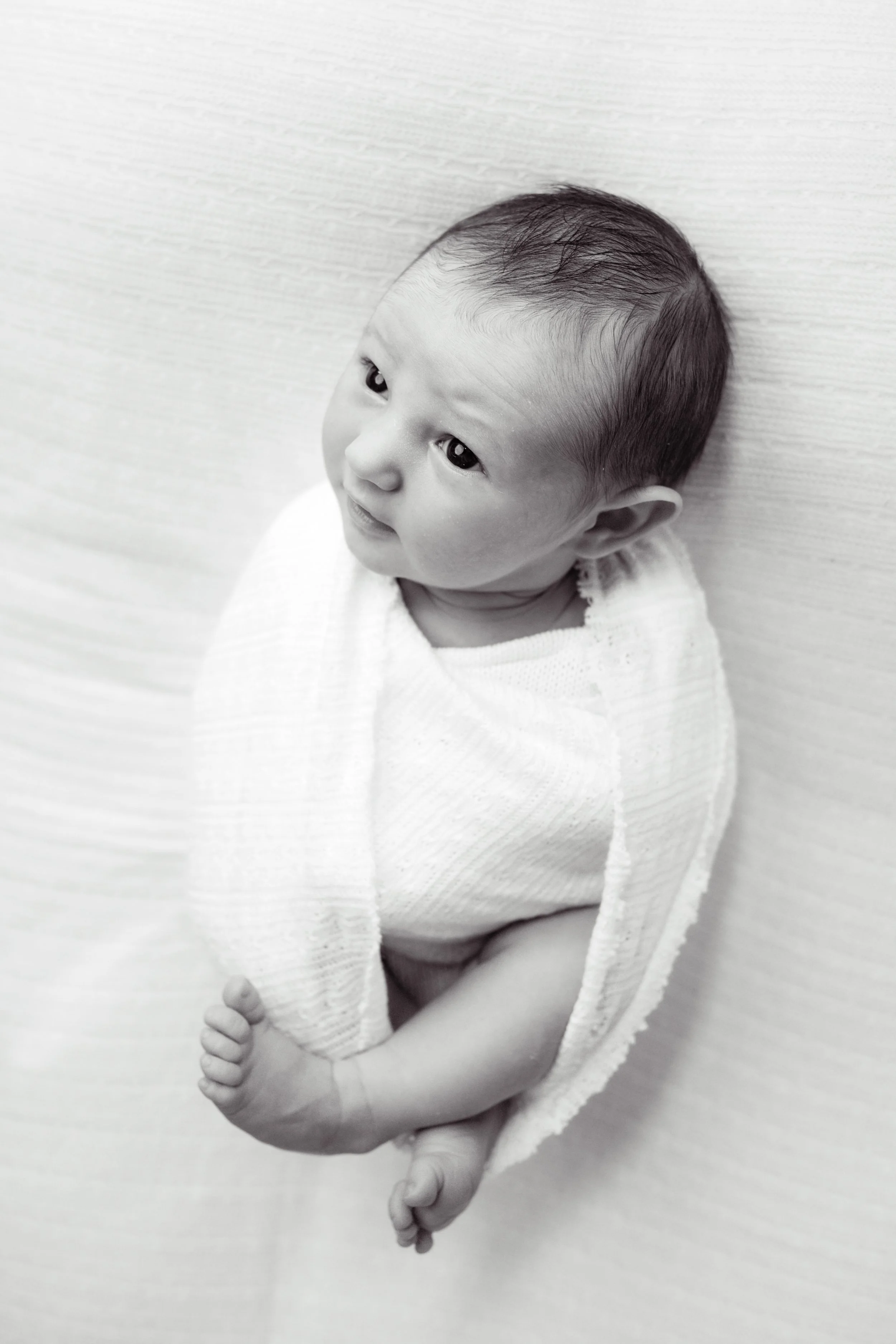 Black and white portrait of a newborn baby wrapped in a soft textured blanket.