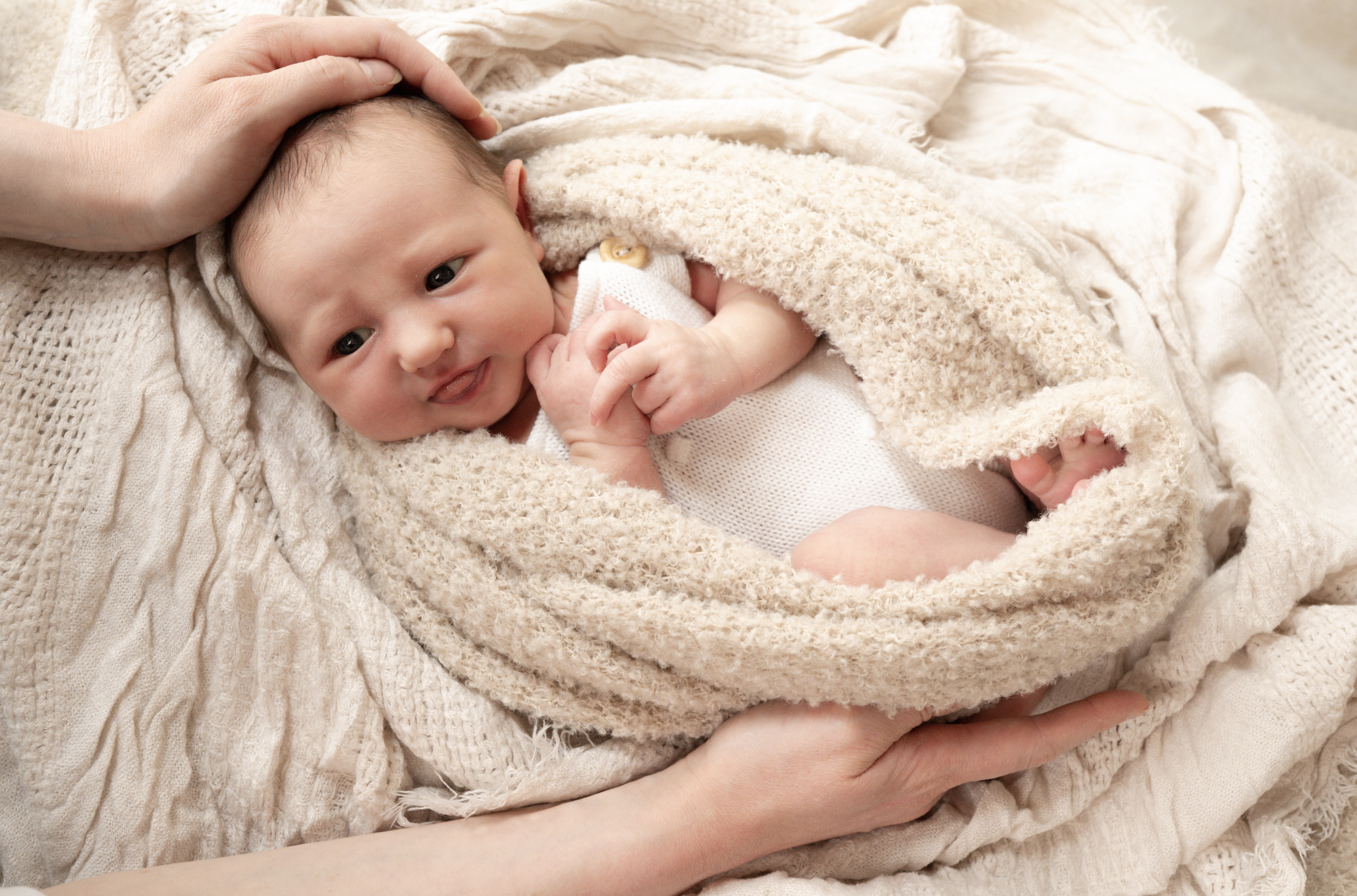 A parent gently holding a swaddled newborn baby in a neutral newborn photography studio.