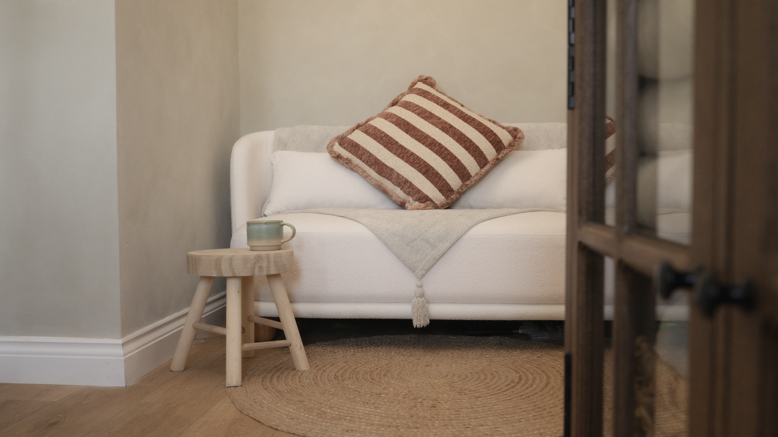Cosy seating area with a white sofa, wooden side table and ceramic mug, creating a calm welcome space inside Little River Photography's studio.