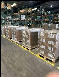 Warehouse with pallets of boxed goods stacked on shelves and on the floor.