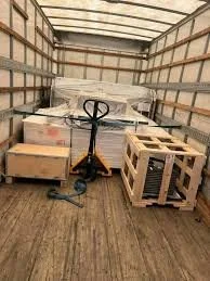 The inside of a truck with wooden pallets, a pallet jack, and boxes loaded inside.