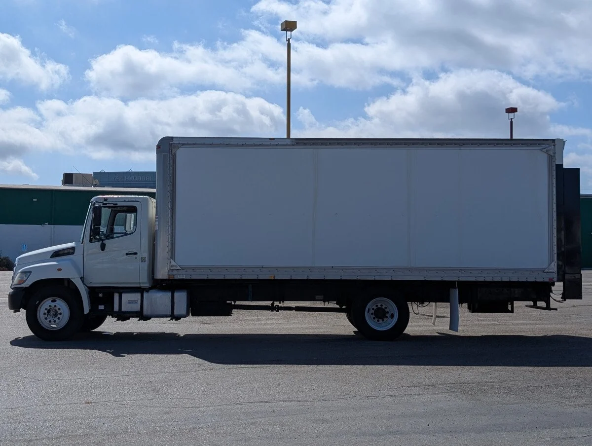 A white box truck parked on an empty paved lot under a partly cloudy sky.