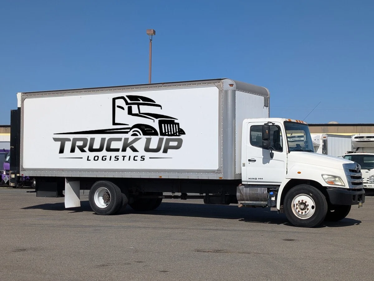 White logistics truck with a logo of a stylized semi-truck and the words 'TRUCK UP LOGISTICS' on the side, parked in a lot on a clear day.