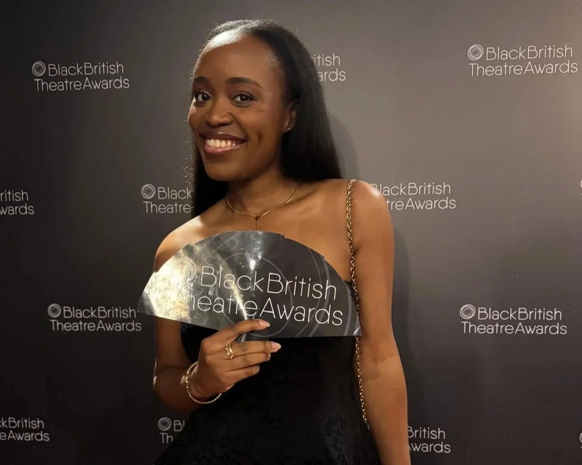 A woman holding sign that reads 'Black British Theatre Awards', smiling in front of a backdrop with the event's name.