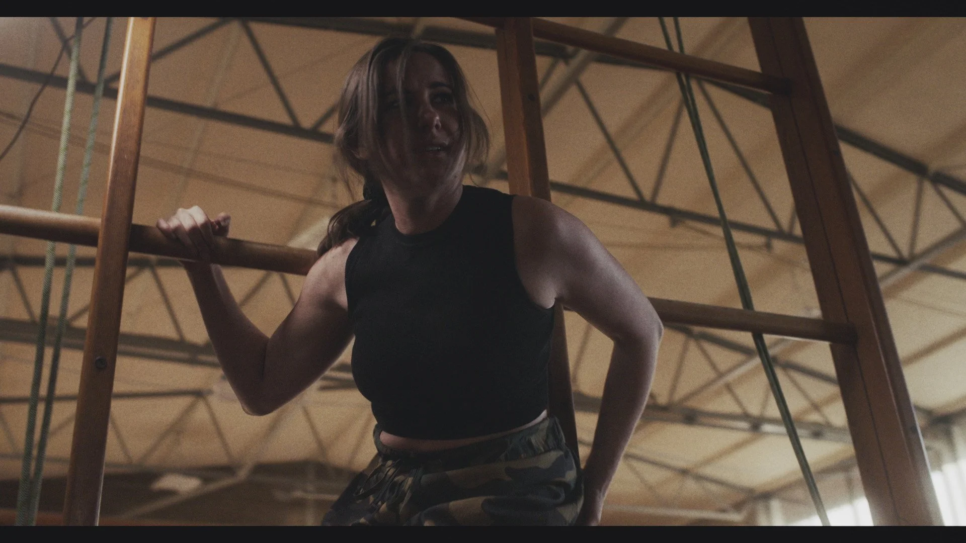 A woman in athletic clothing holding onto a wooden climbing gym.