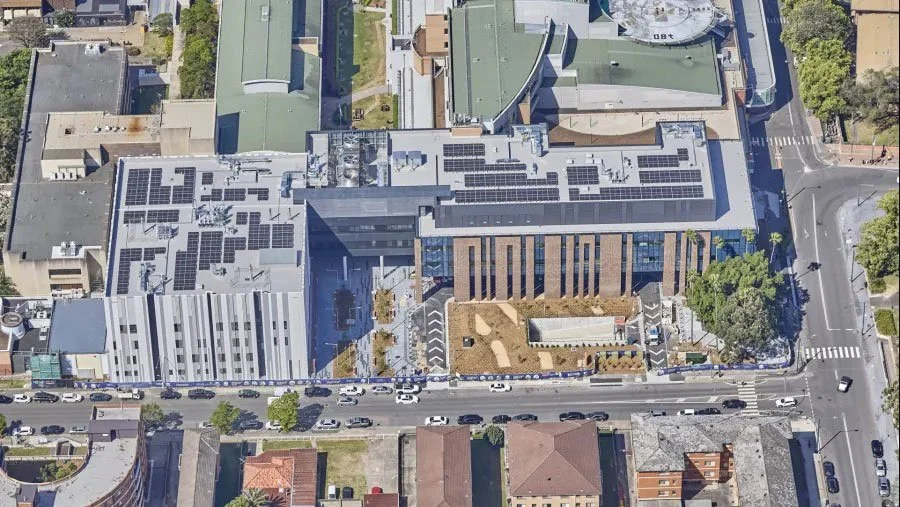 Aerial view of a city block with commercial buildings, some with solar panels on the roofs, and a street filled with parked and moving cars.
