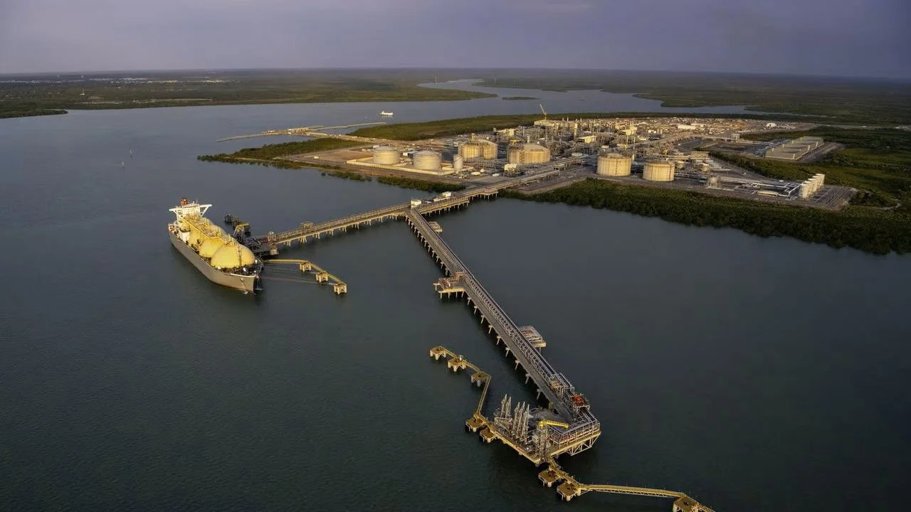 A large industrial harbor with a cruise ship docked at a pier, surrounded by storage tanks and industrial buildings.