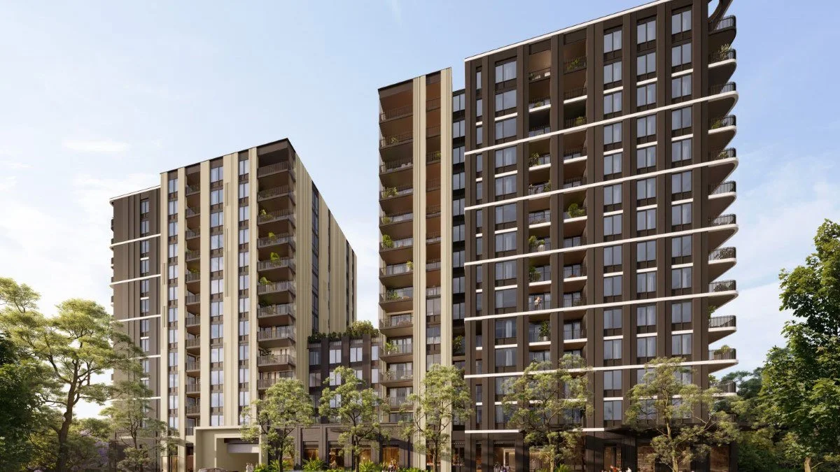 Two modern high-rise apartment buildings with balconies, surrounded by trees under a blue sky.