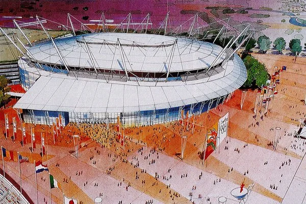 A large stadium with a white roof and tall support beams, surrounded by an open plaza with many small groups of people, flags, and some trees in the background.