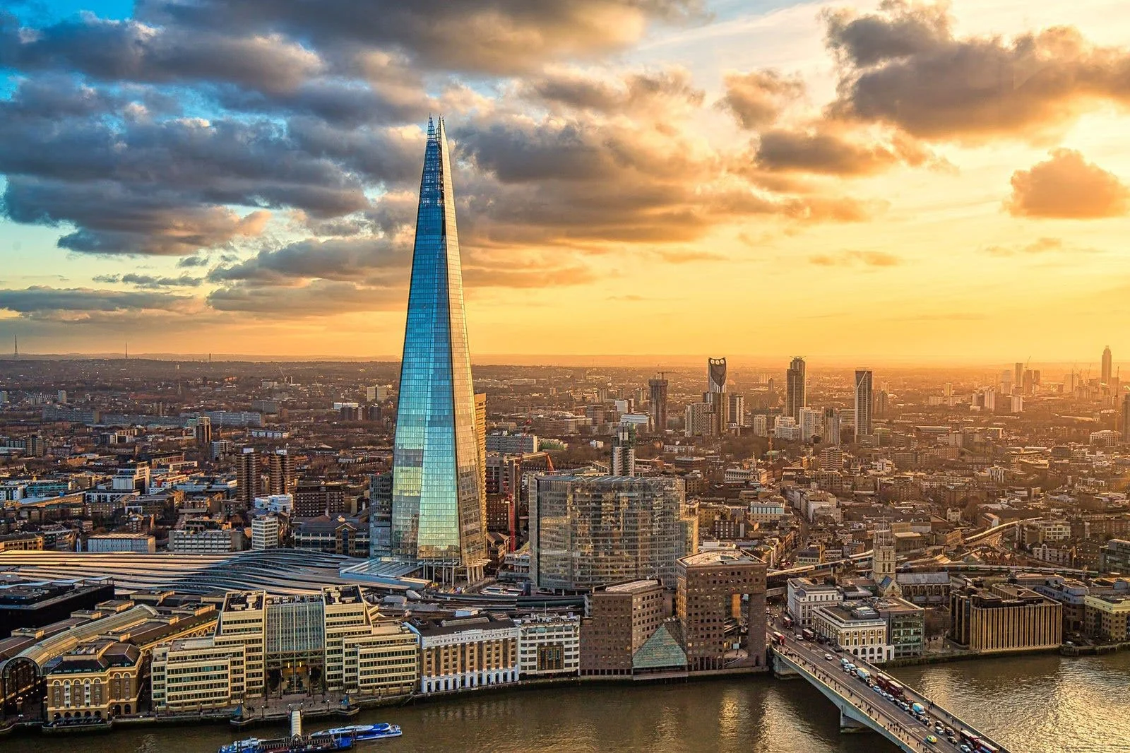 Aerial view of London skyline at sunset with The Shard skyscraper, river Thames, and city buildings.